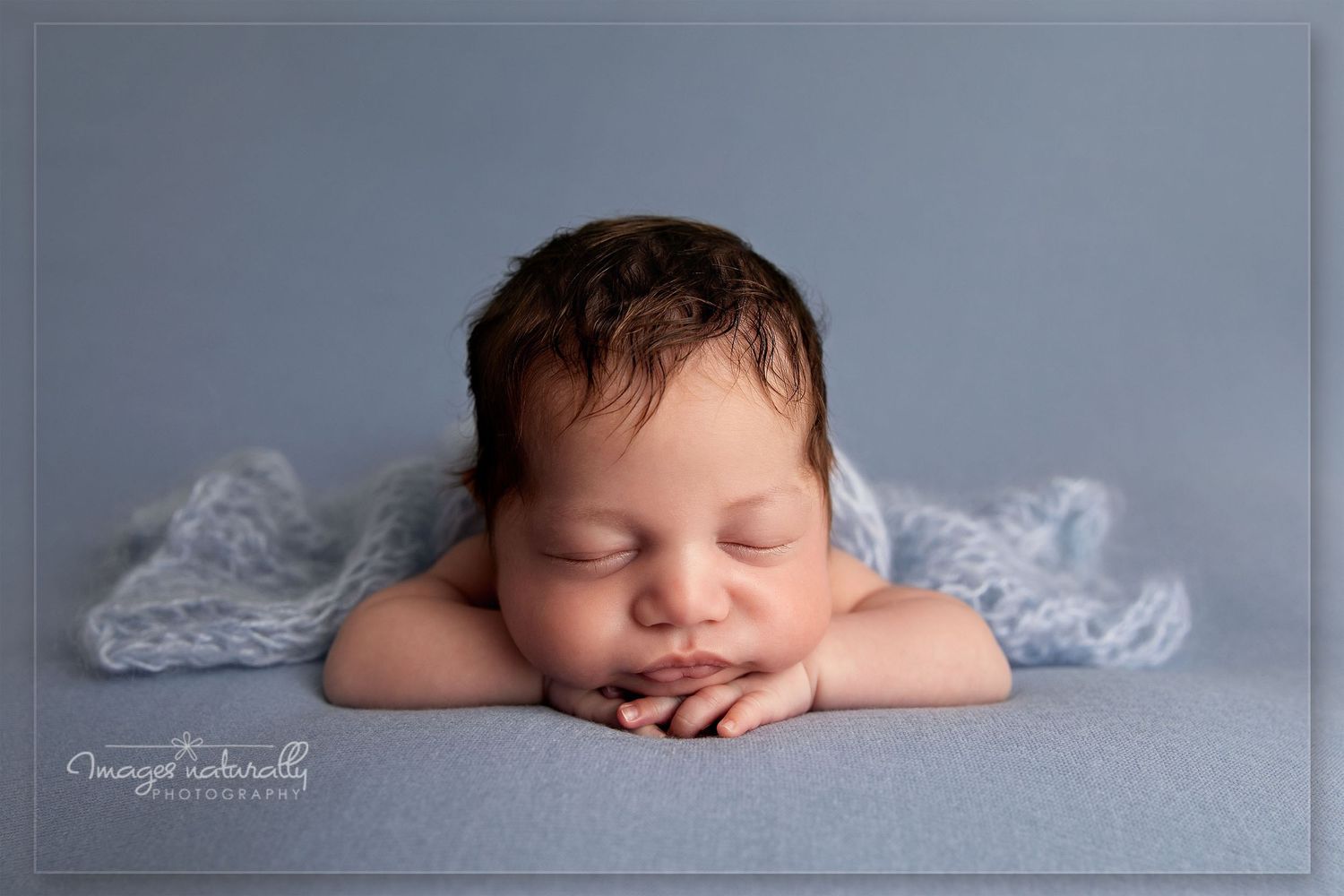 Sleeping newborn baby in soft blue and gray tones lying on textured blanket during professional photo session.
