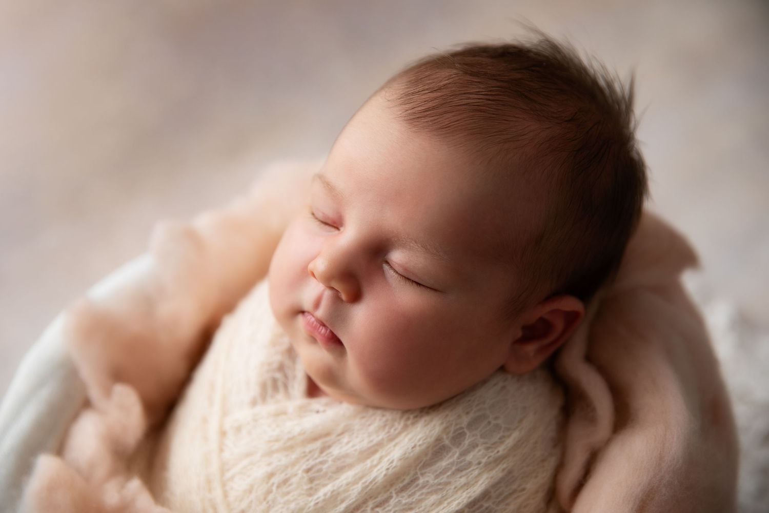 A sleeping newborn baby wrapped in soft white fabric lies peacefully on a cozy blanket.