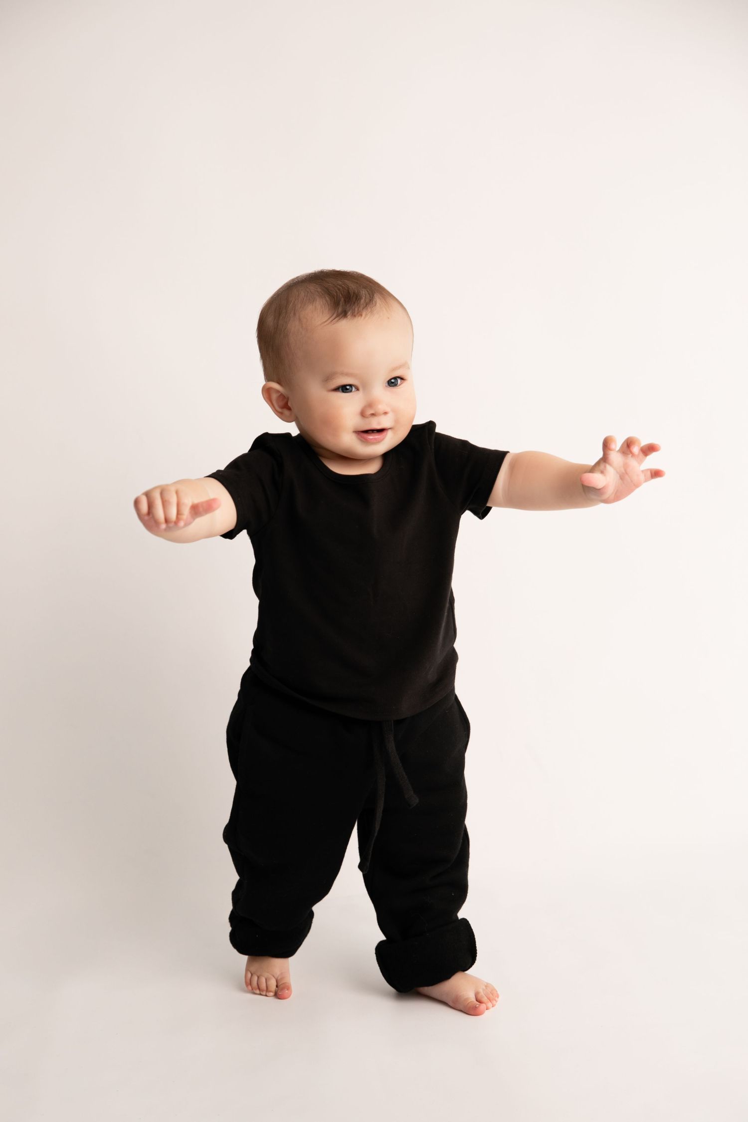 Baby wearing black outfit makes playful poses against white background in four sequential photos.