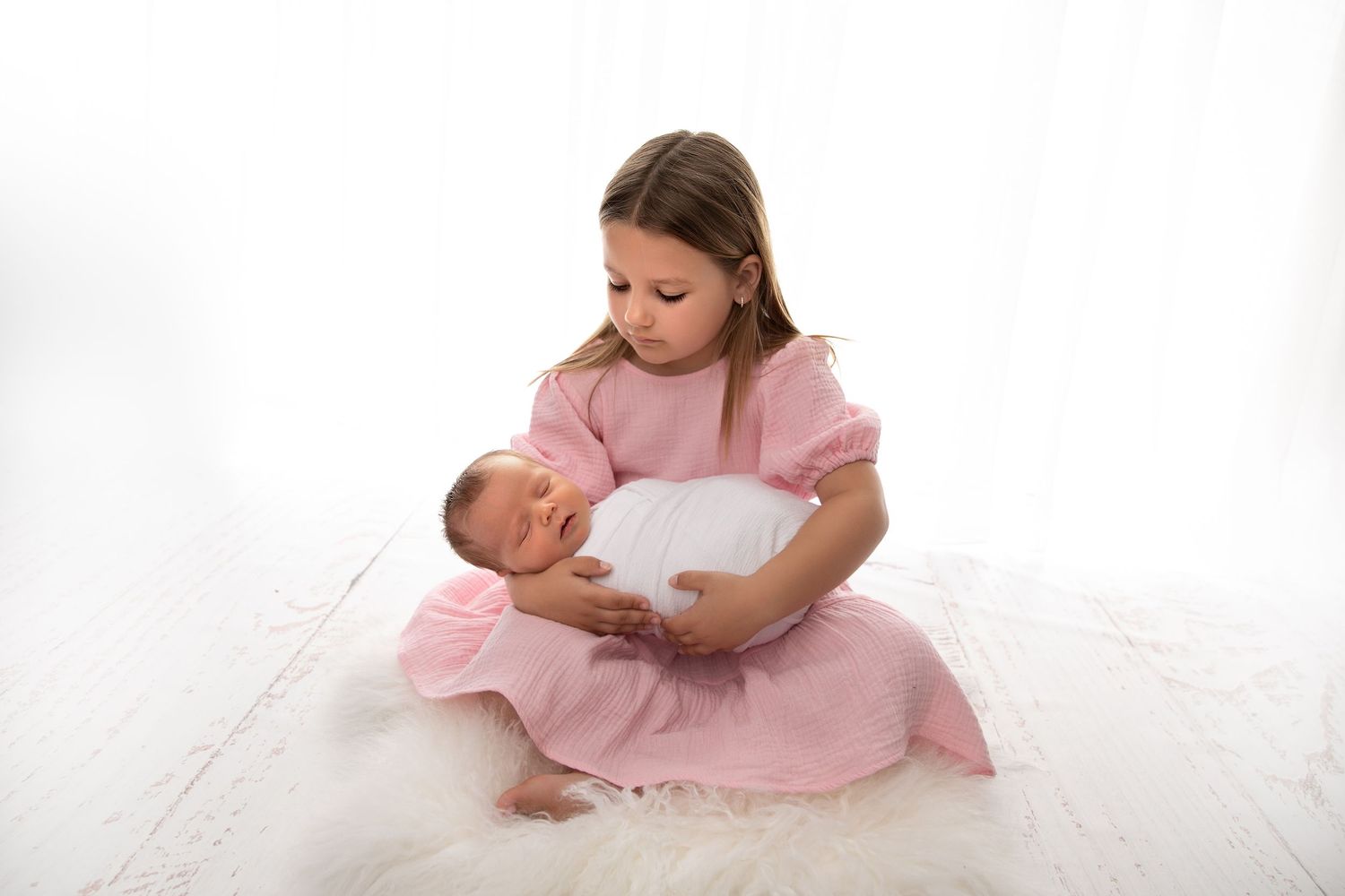 A person in a pink dress sits on a white floor with a baby, shown in a series of tender nurturing moments.