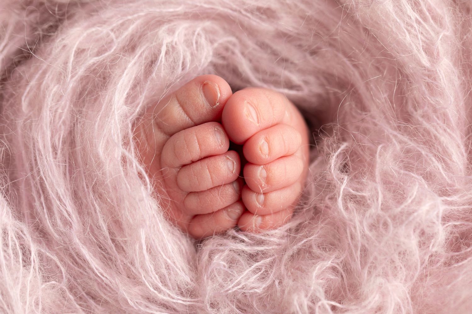 A close-up photo of a newborn baby's tiny feet with pink skin against a soft white blanket background.