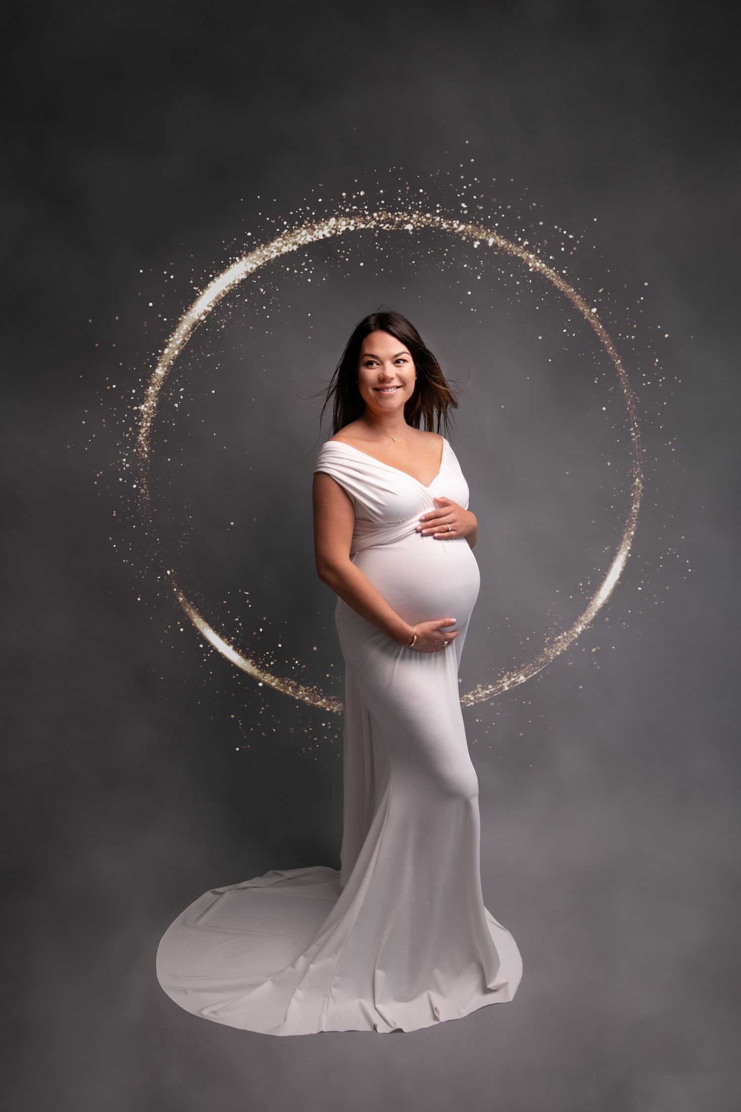 Maternity photoshoot featuring a flowing white dress against a dark gray background with glowing circular light effects.