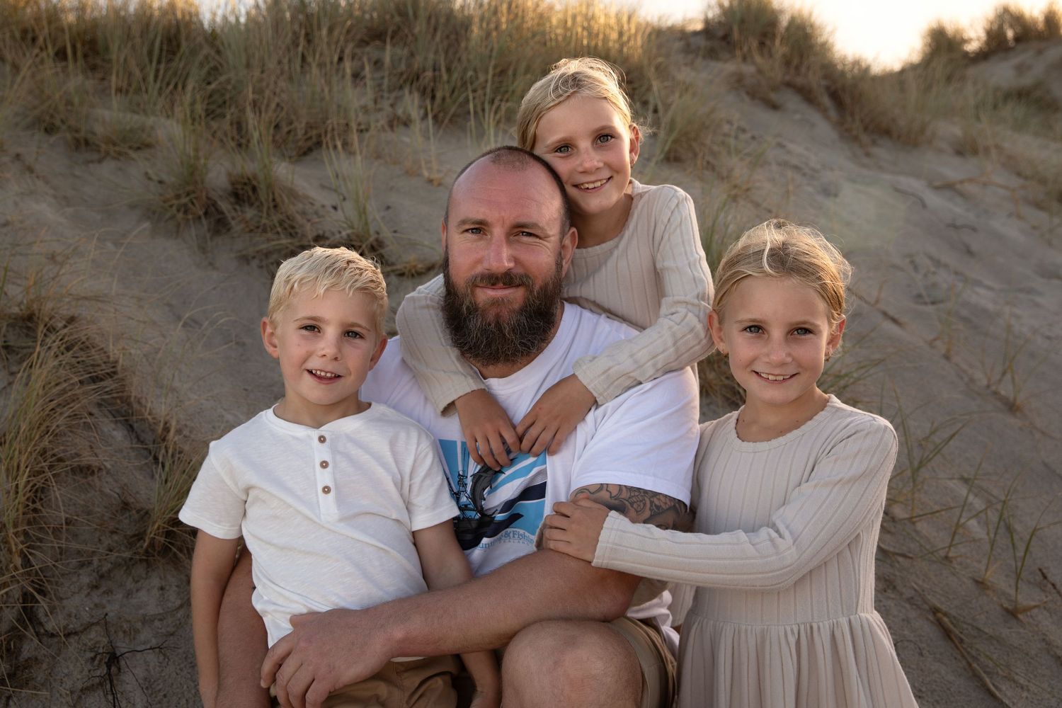 A family sits together on sandy dunes during golden hour at the beach.