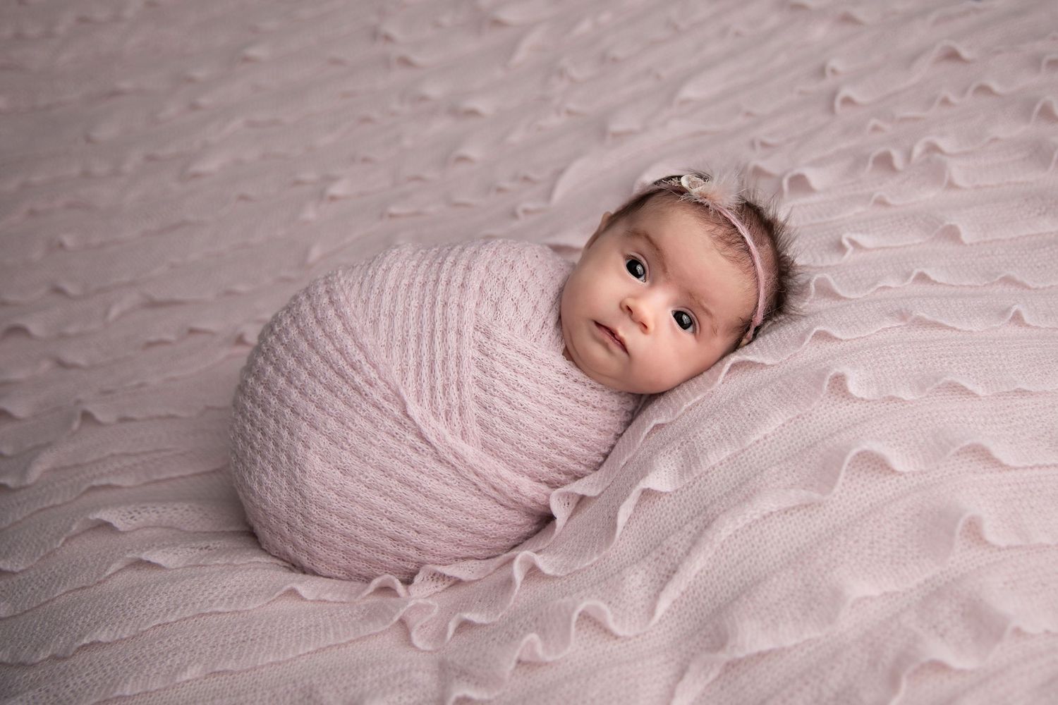 A series of soft, dreamy newborn photos showing a baby wrapped in pink swaddle on textured white bedding.