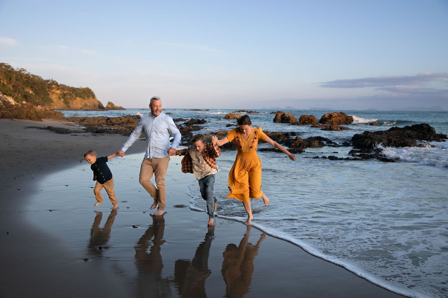 A group plays and dances together at sunset on a rocky beach with waves crashing against the shore.