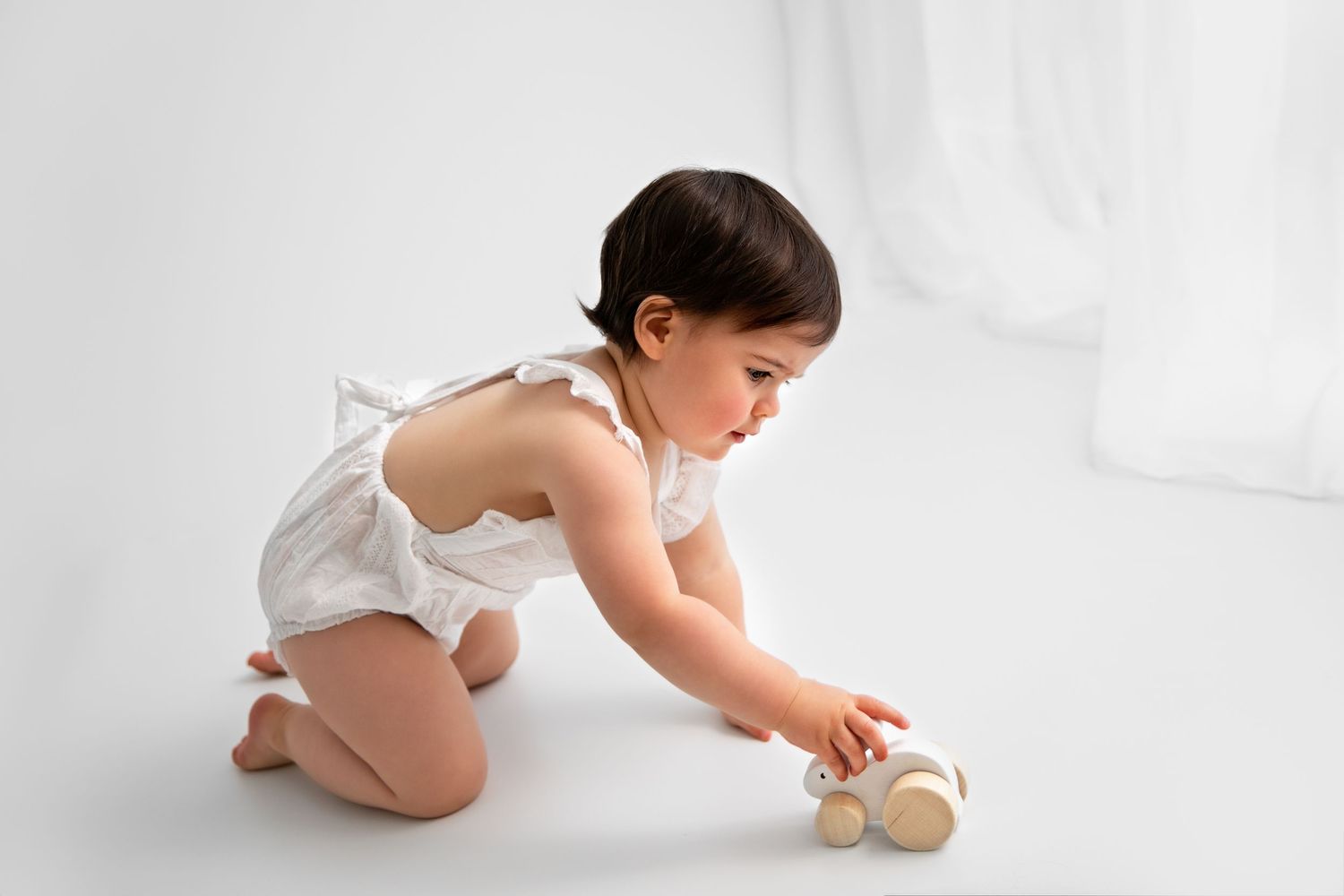 Baby in white diaper crawls across white backdrop reaching for wooden toy in progression sequence.
