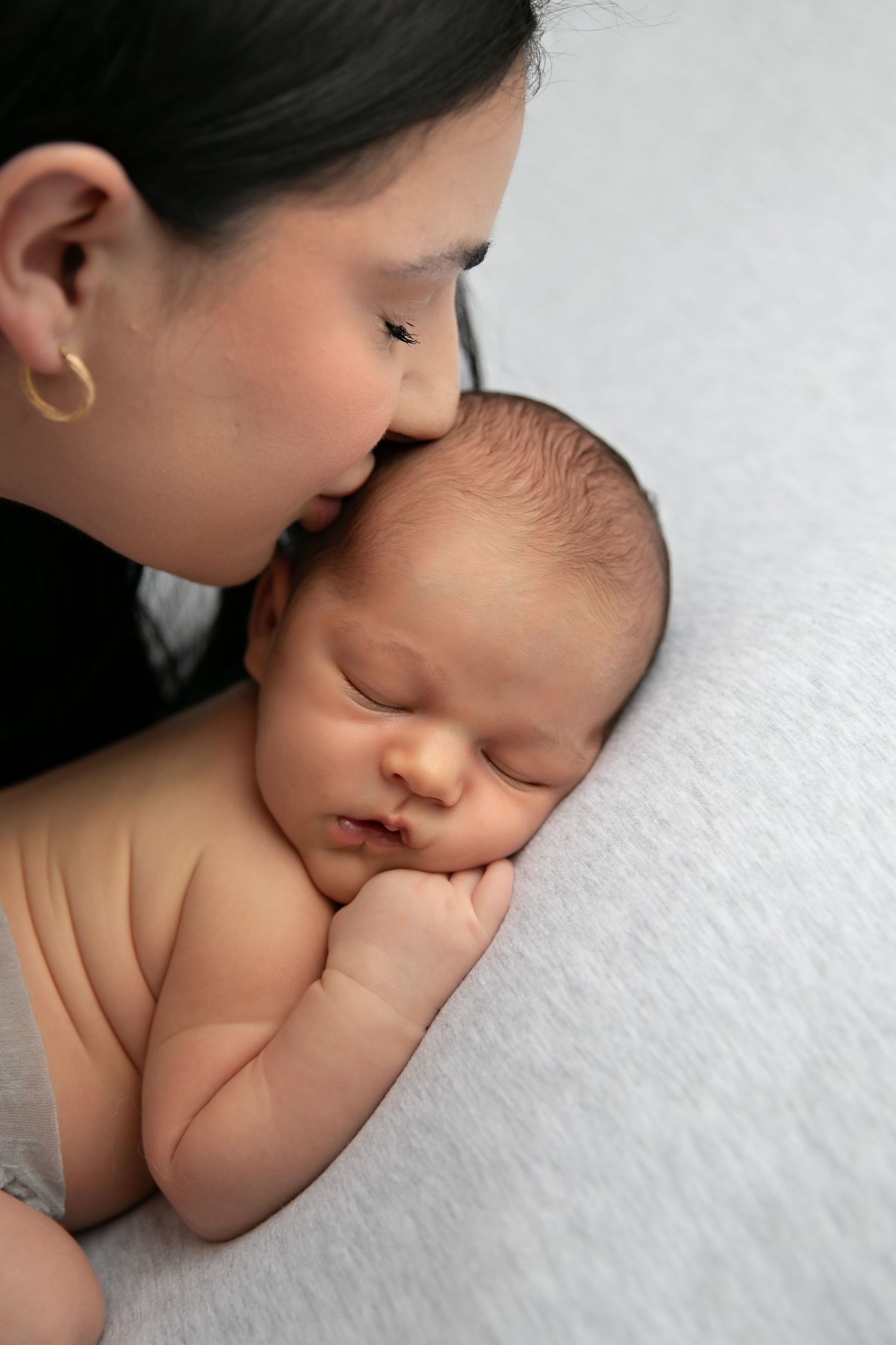 A series of tender moments showing a parent kissing a sleeping newborn baby on white bedding.