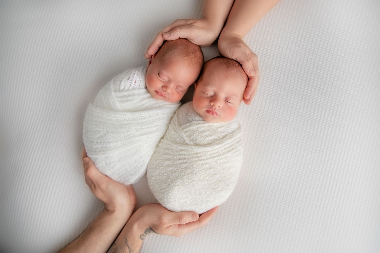 Sleeping newborn baby wrapped in white blanket lying on soft gray background during professional photo session.