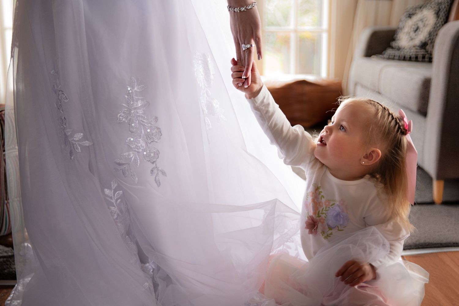 A little girl in a white dress twirls and dances gracefully through a sunlit room with sheer curtains.