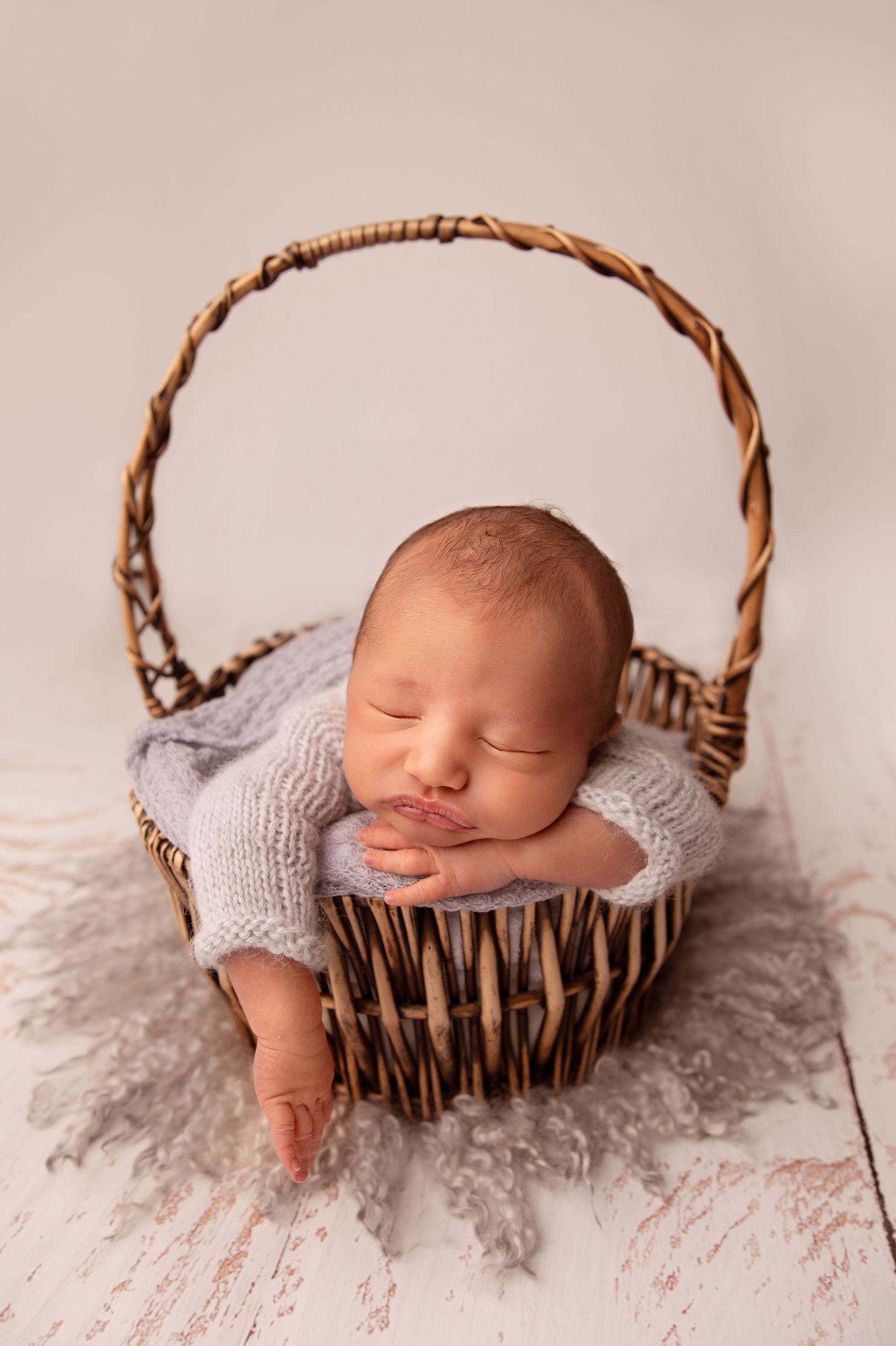 Sleeping newborn rests peacefully in a rustic woven basket with soft gray blankets.