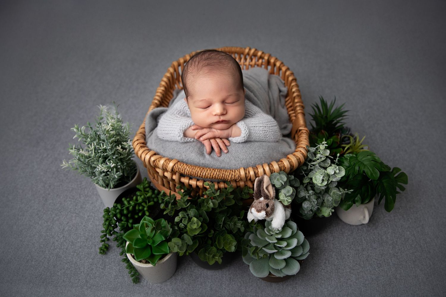 Newborn photography collage showing baby sleeping in wicker baskets with greenery and floral arrangements on grey backdrop.