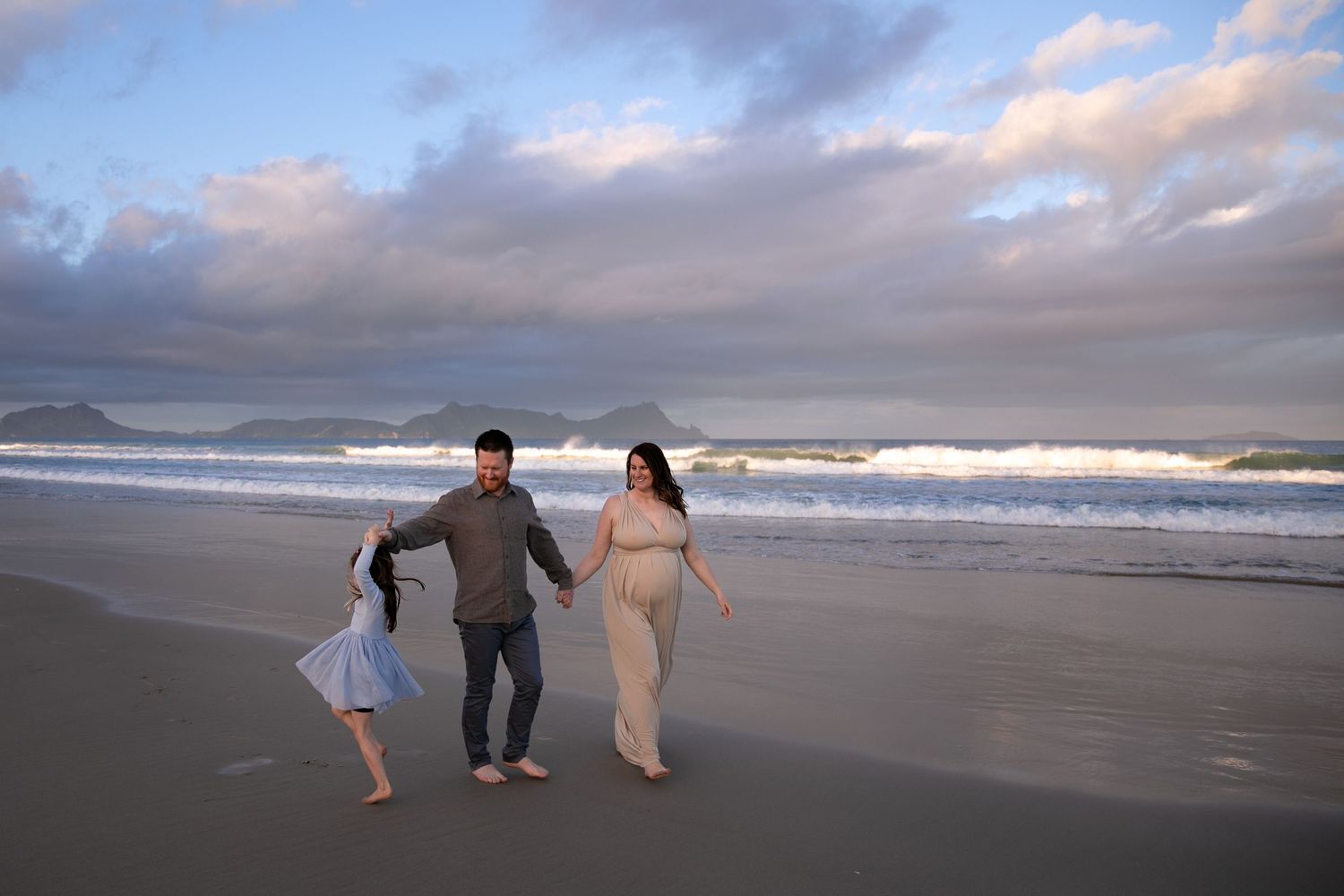 People walking along a misty beach shoreline with waves and cloudy skies in the background.