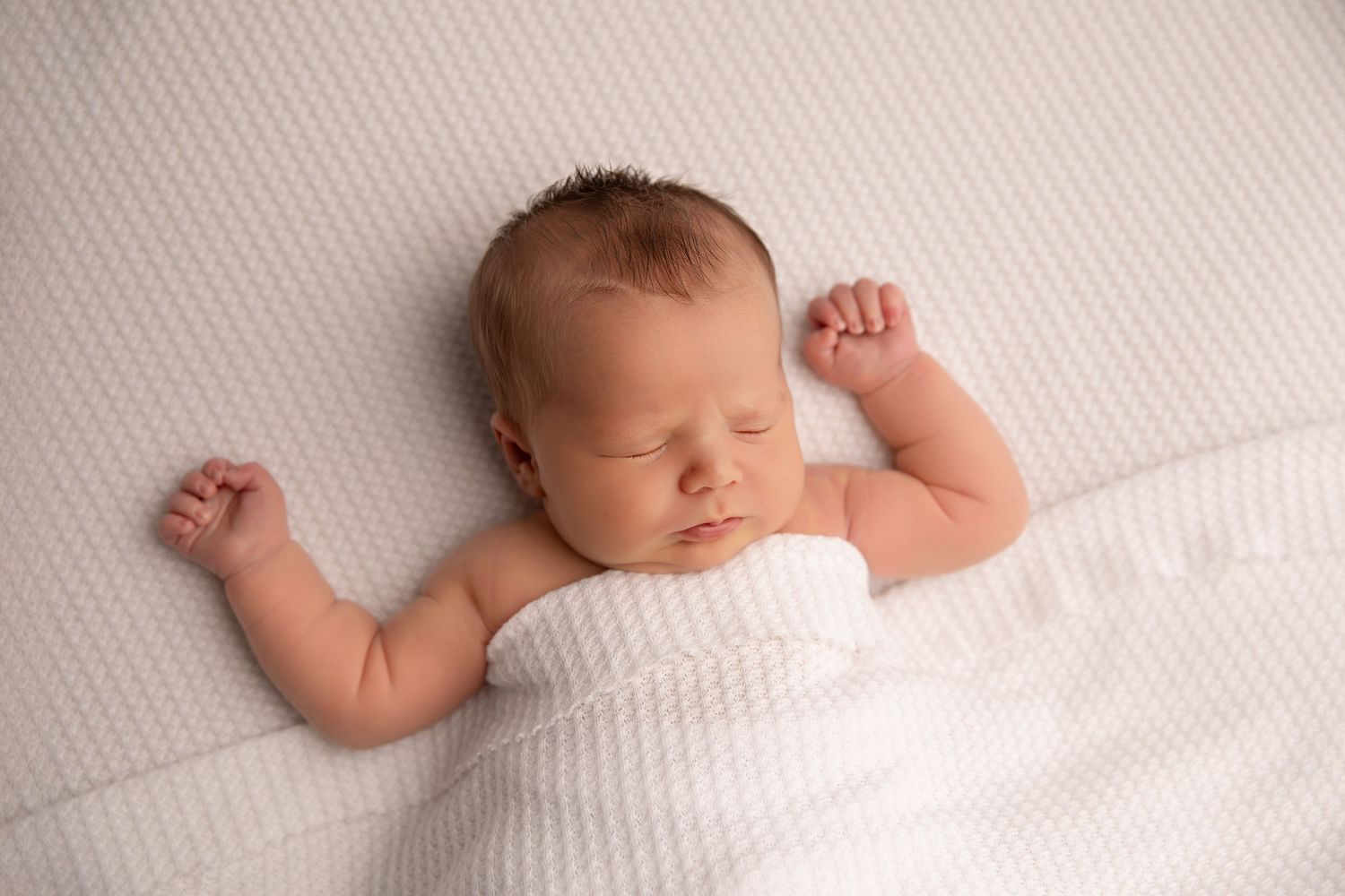 A sleeping baby lies peacefully on white bedding in a series of connected photographs.