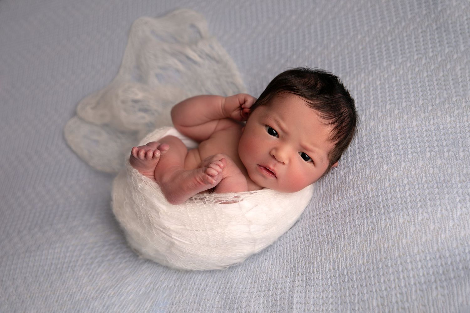 A sleeping newborn baby wrapped in white fabric photographed from different angles.