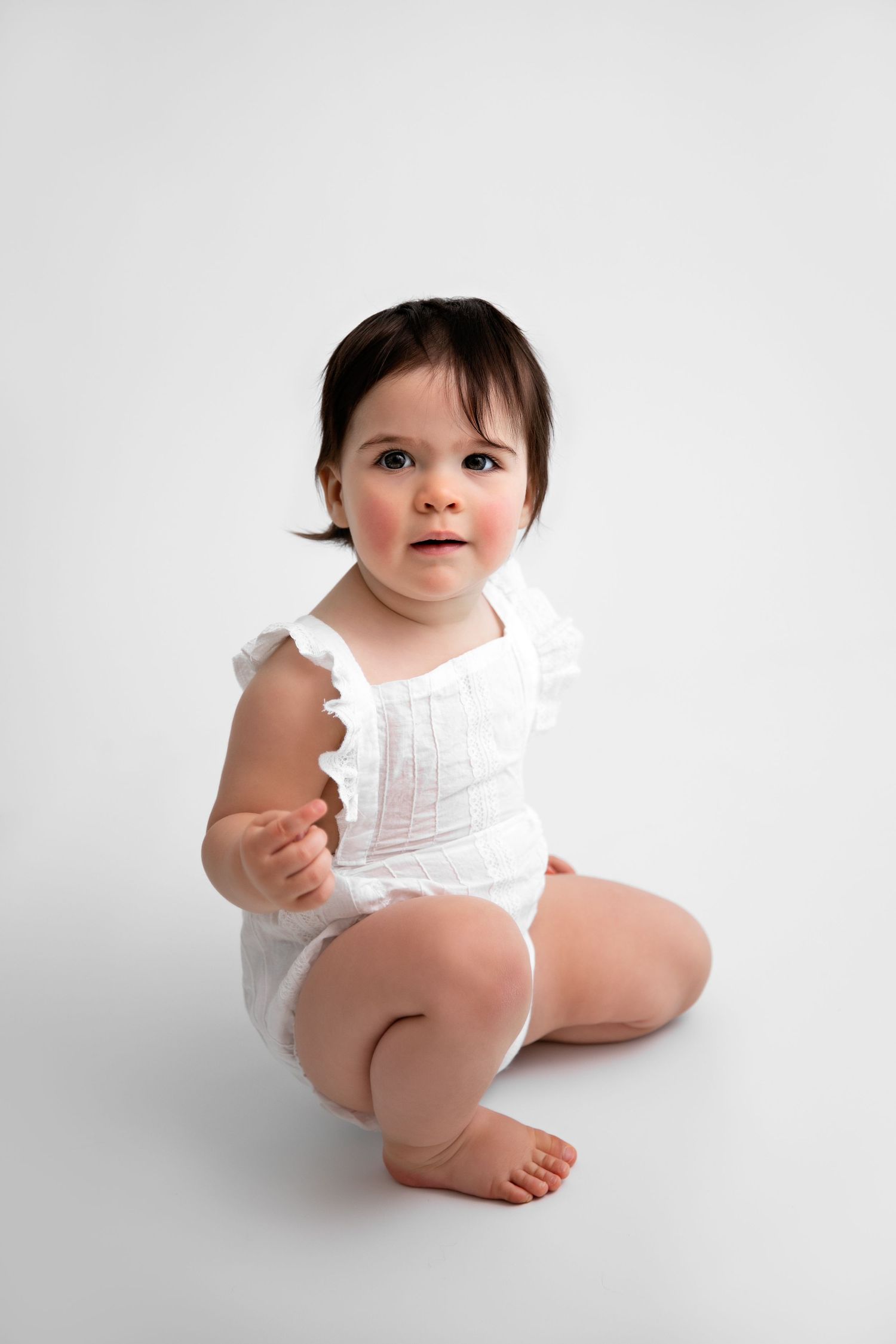 Baby in white ruffled outfit sitting on white background in three similar poses.