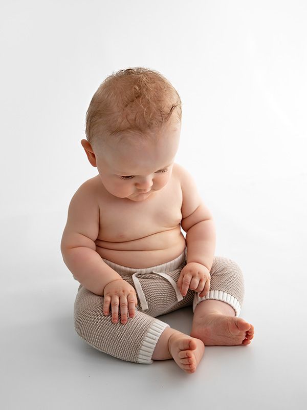 Baby wearing knit shorts sits on white background during studio portrait session.