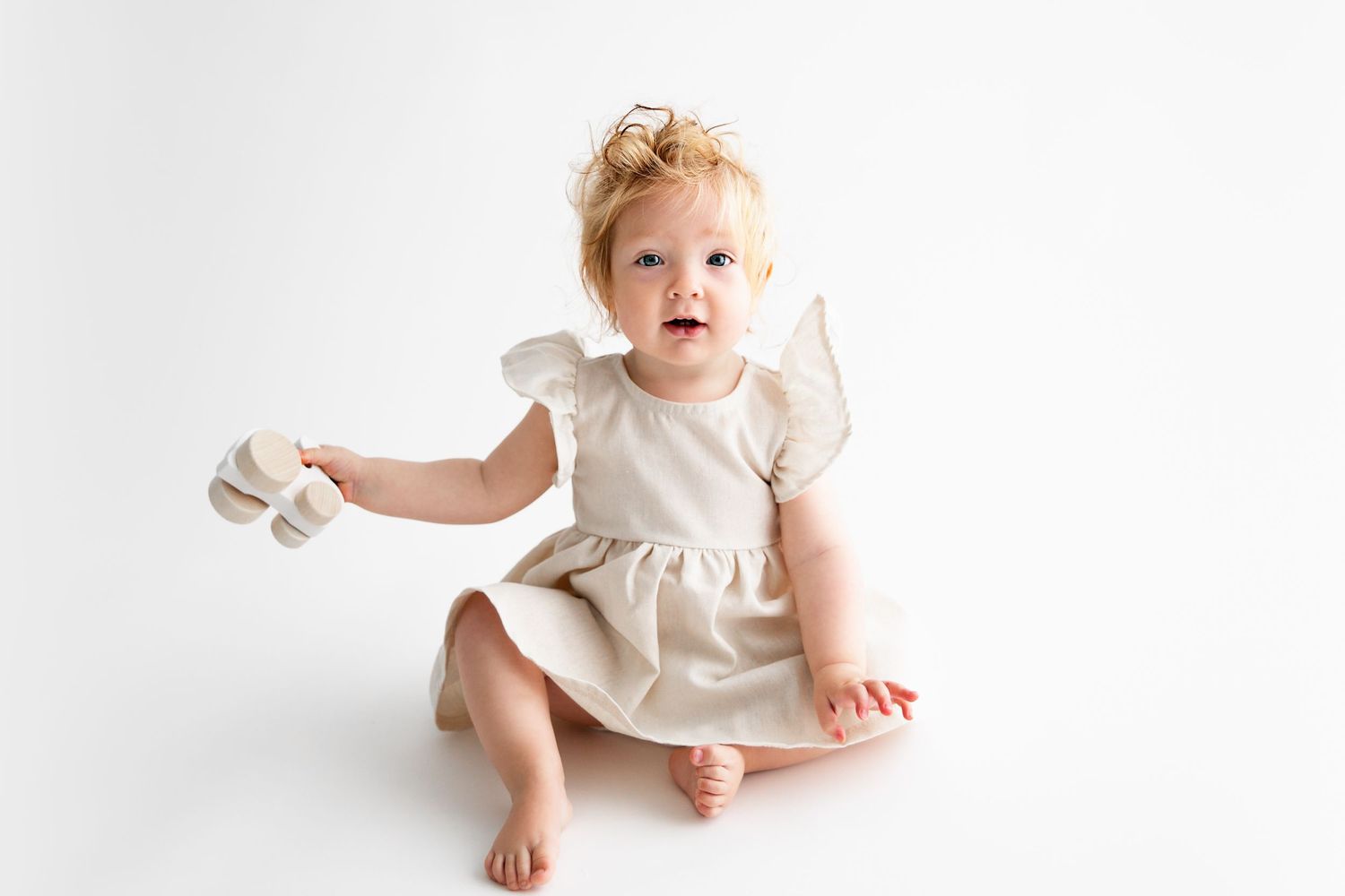 Baby in white ruffled dress poses during studio photoshoot.