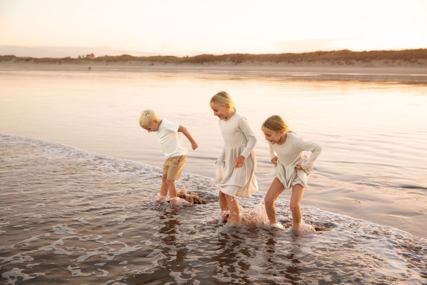 Family enjoying time together in shallow ocean waters at sunset.