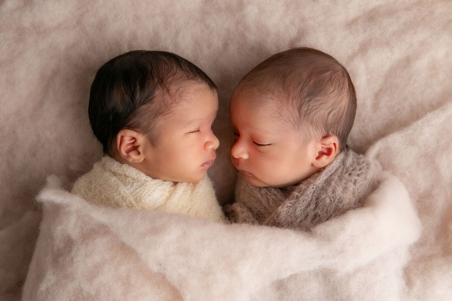 Two sleeping newborn babies lying together on soft white blankets in various peaceful poses.