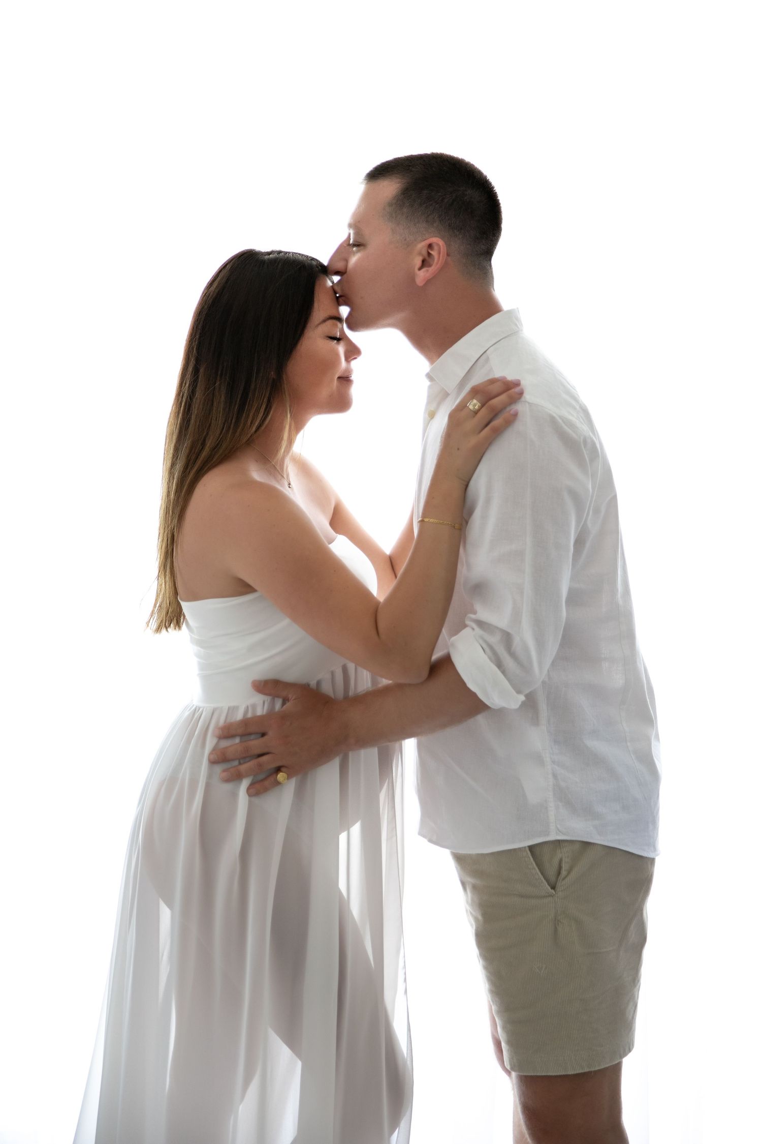 Romantic couple in white clothing embraces in a series of intimate poses against white background.