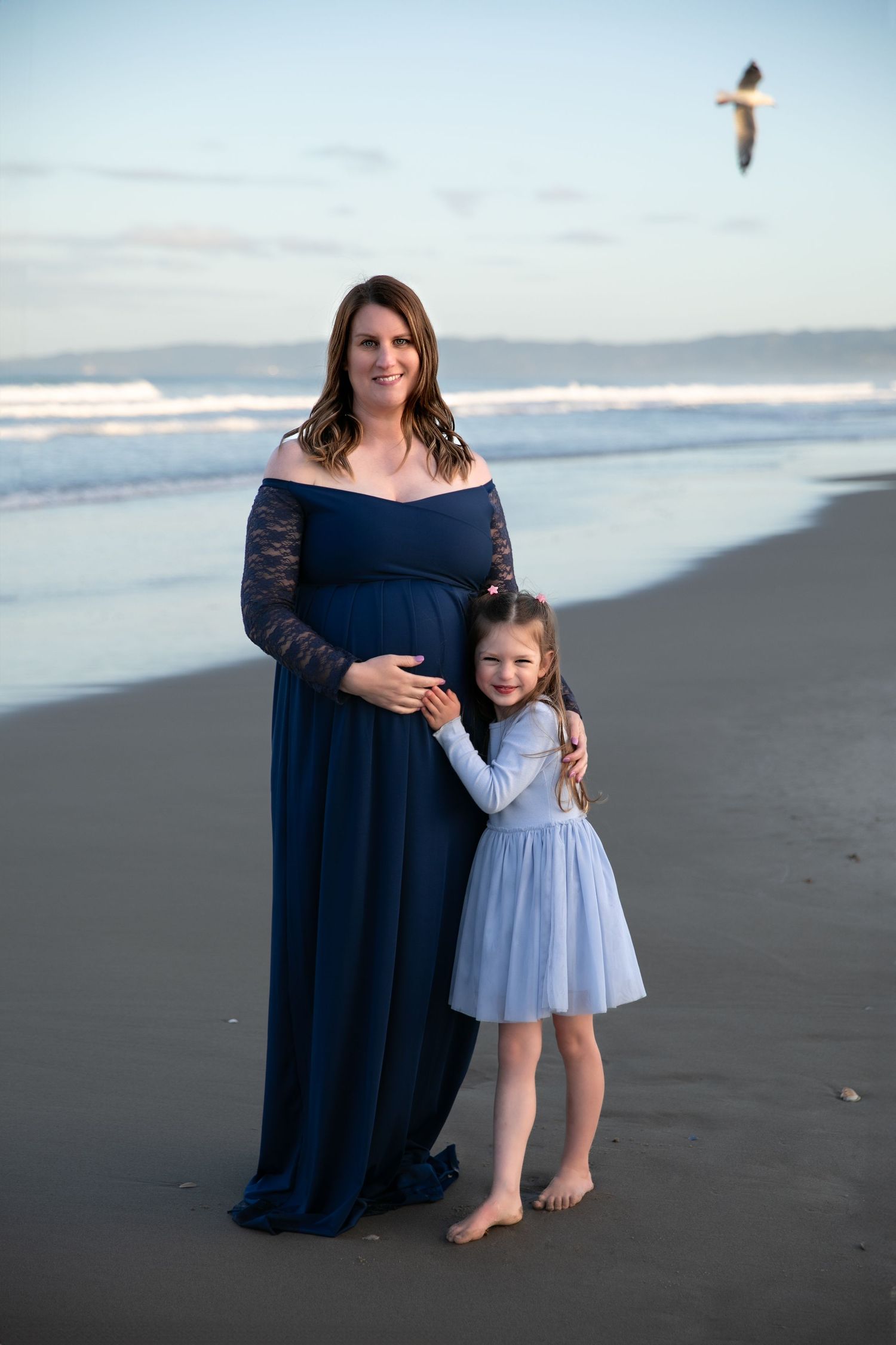 Two people in coordinating blue dresses stand together on a beach at sunset.
