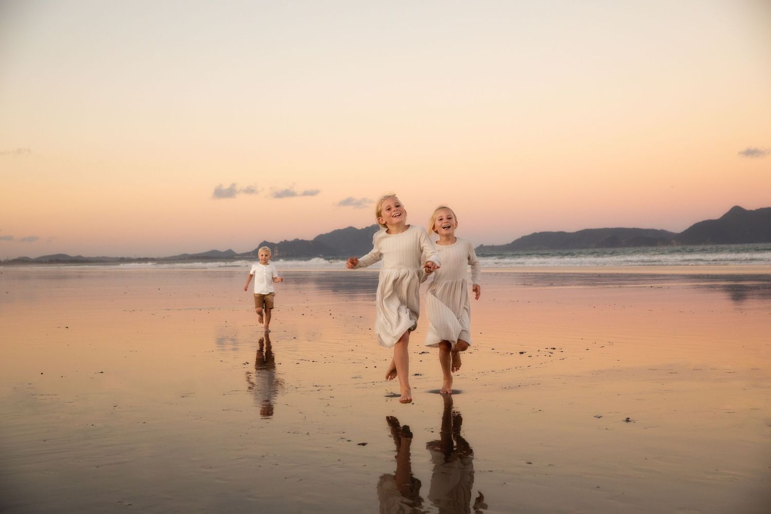 A family walks along a scenic beach at sunset with their dog while waves gently lap at the shore.