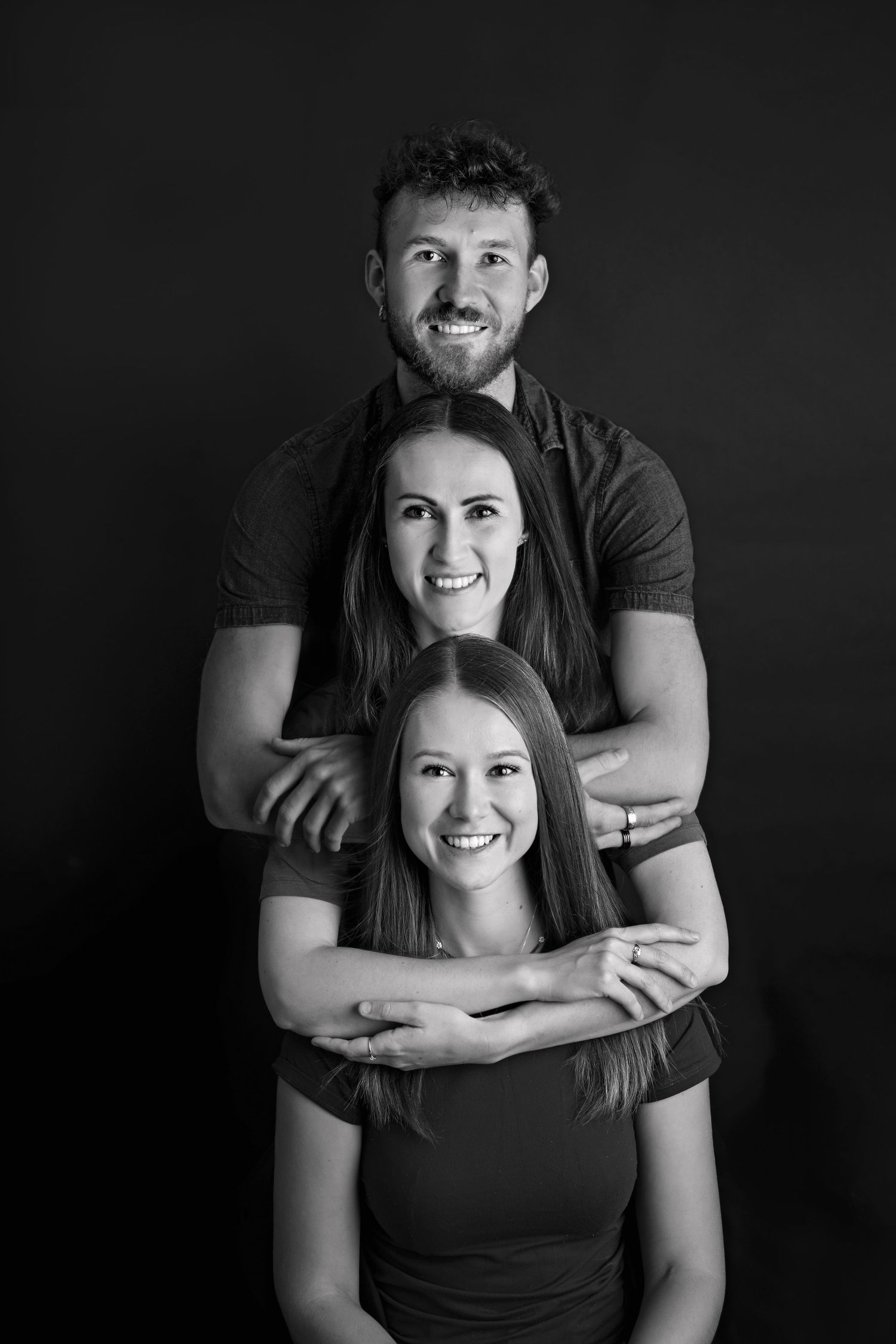 A black and white portrait series showing a couple embracing and smiling against a dark background.