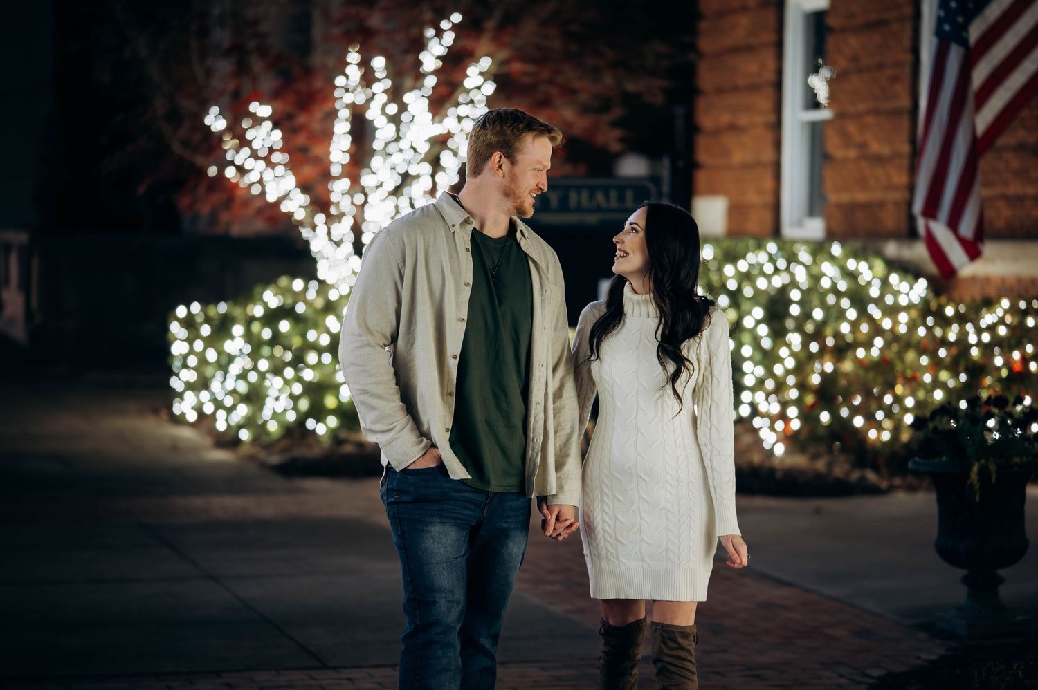 Happy couple holding hands and smiling at each other near Christmas light display.