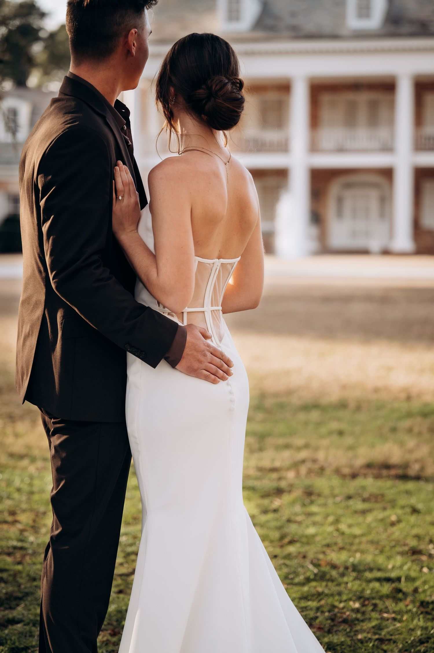 Couple in wedding attire embracing near colonial style architecture.