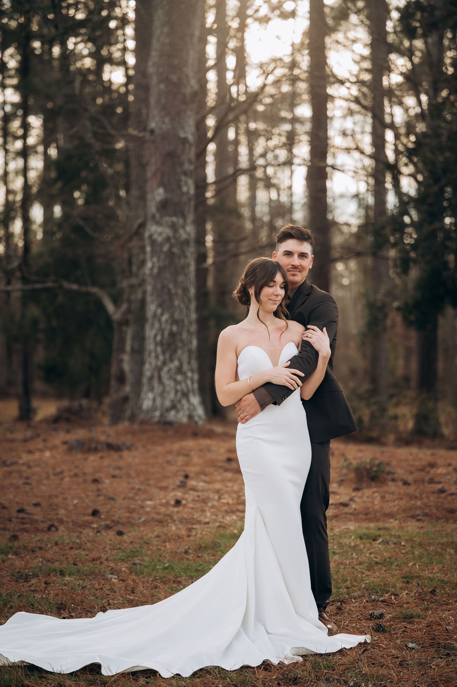 A romantic wedding photo series in a forest setting with a flowing white dress and formal attire at sunset.