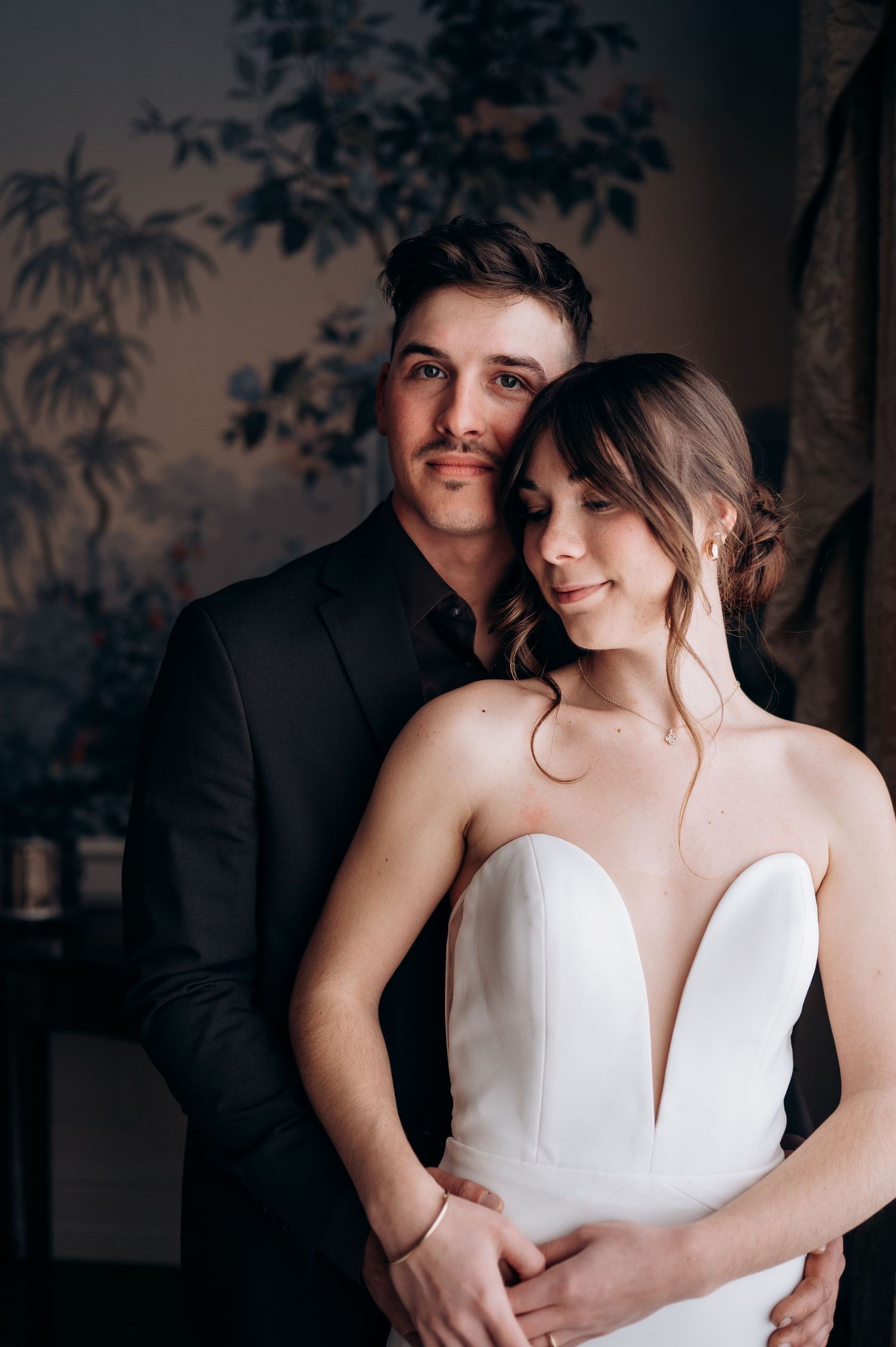 Elegant couple poses together, with the bride wearing a white strapless gown and the groom in a dark suit.