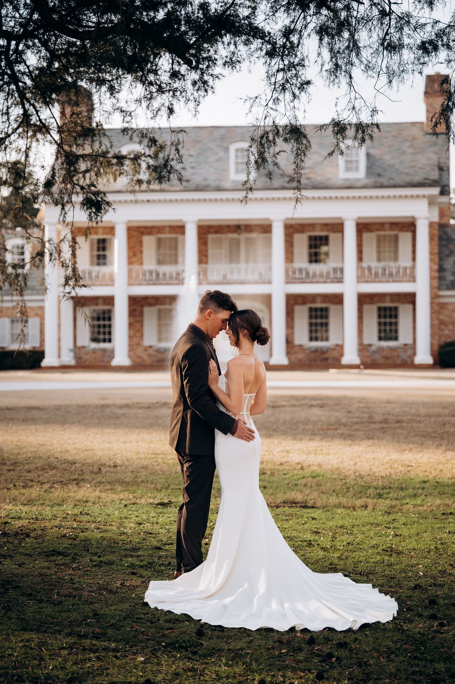 Newlyweds pose in front of a stately colonial building with white columns and brick facade.