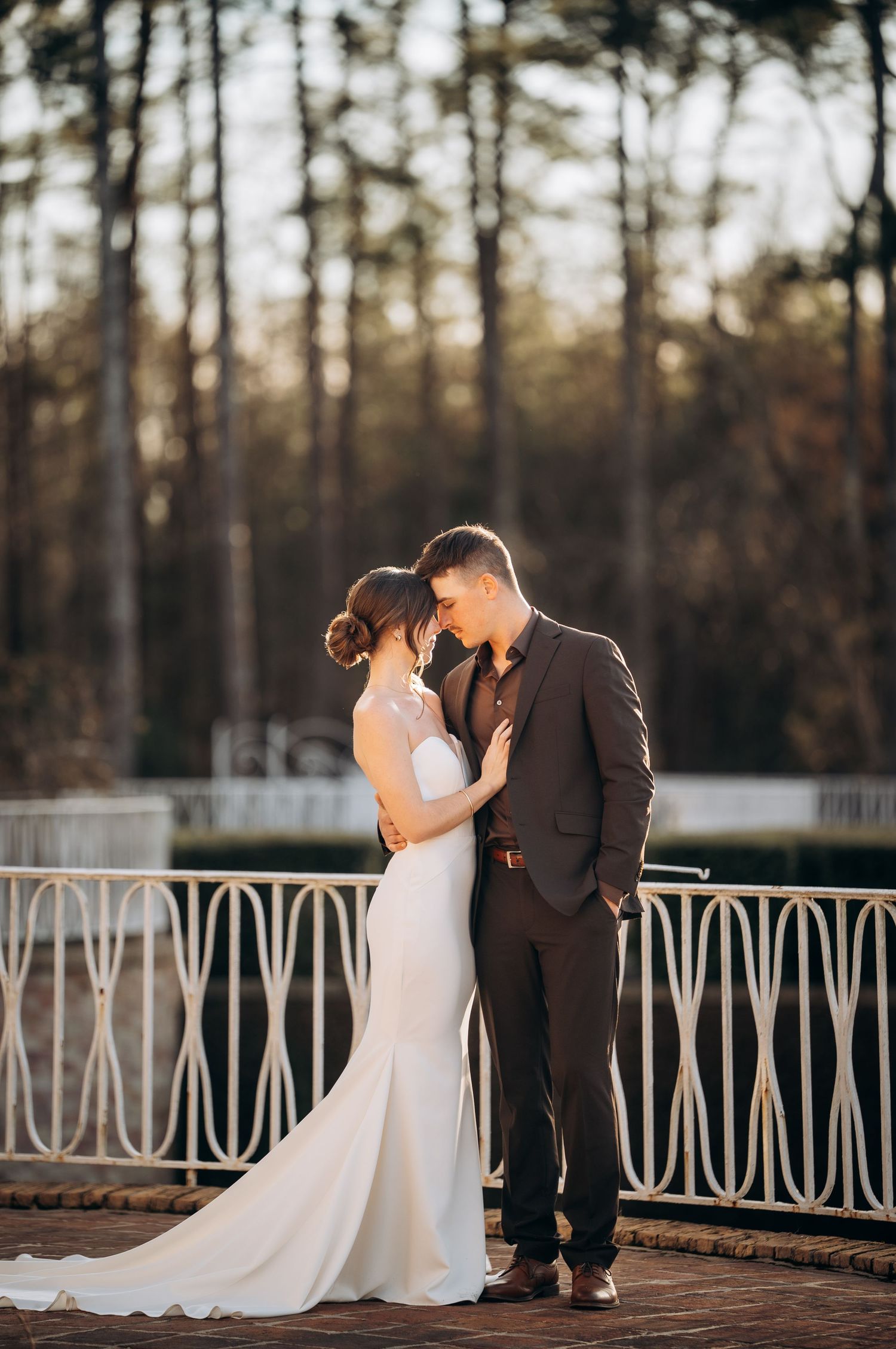 Sunset wedding portrait on white iron balcony surrounded by pine trees.
