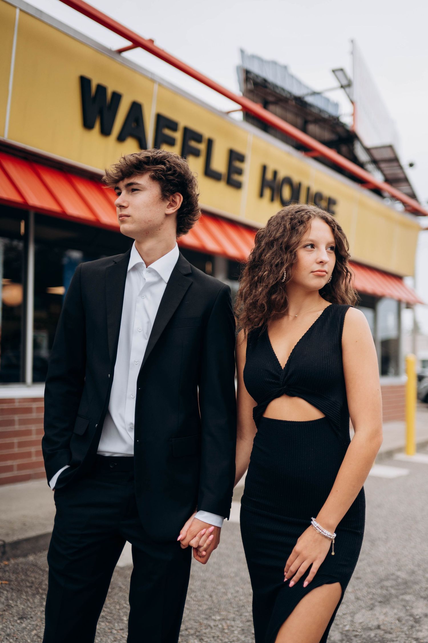 Stylish couple in black outfits standing outside Waffle House at night.