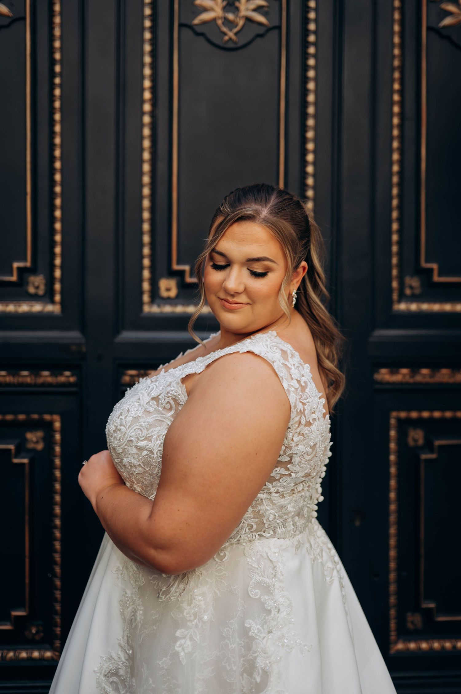 Beautiful lace wedding dress details shown against ornate black doors in an elegant setting.