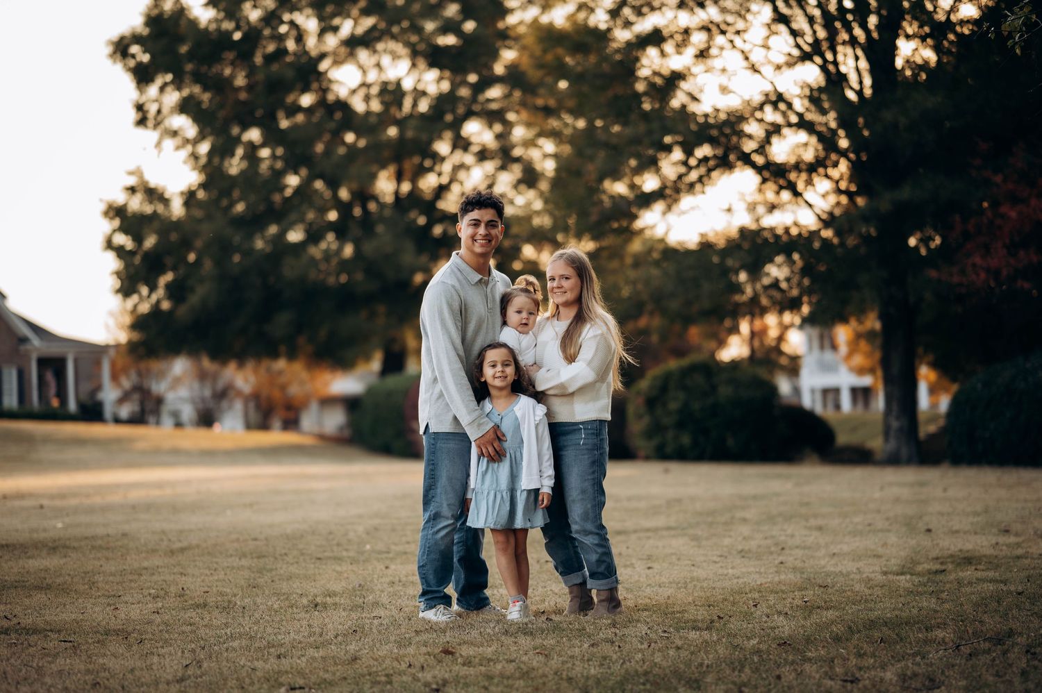 A family of three poses together at sunset in a grassy field.