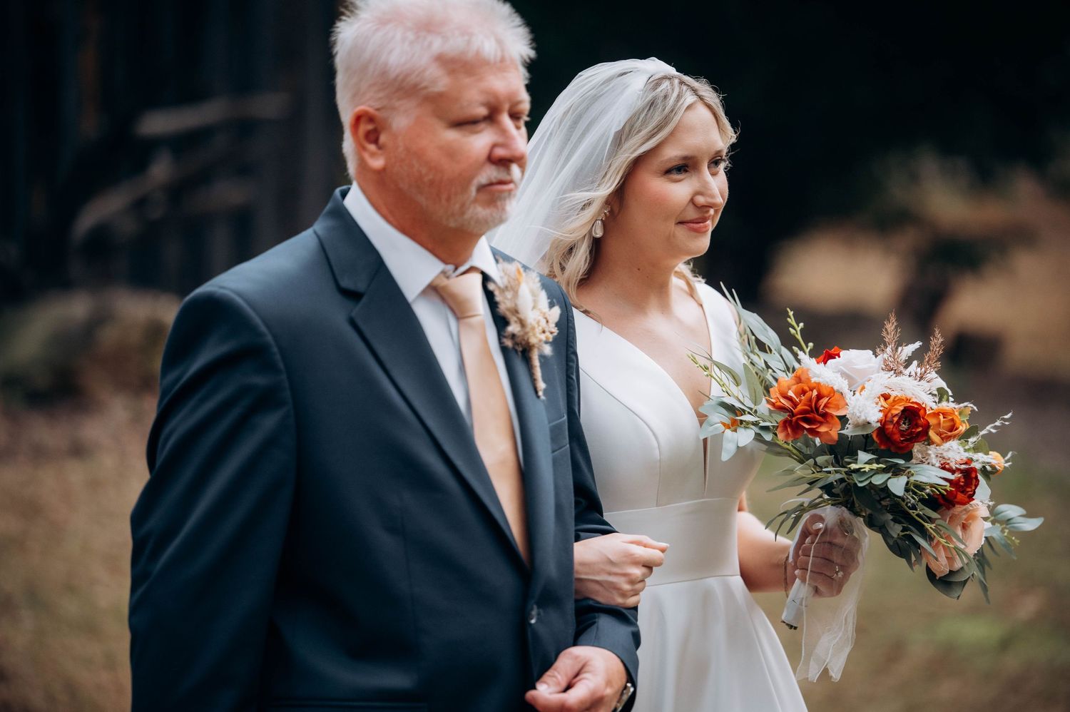 Wedding party members walking outdoors with autumn foliage in background.