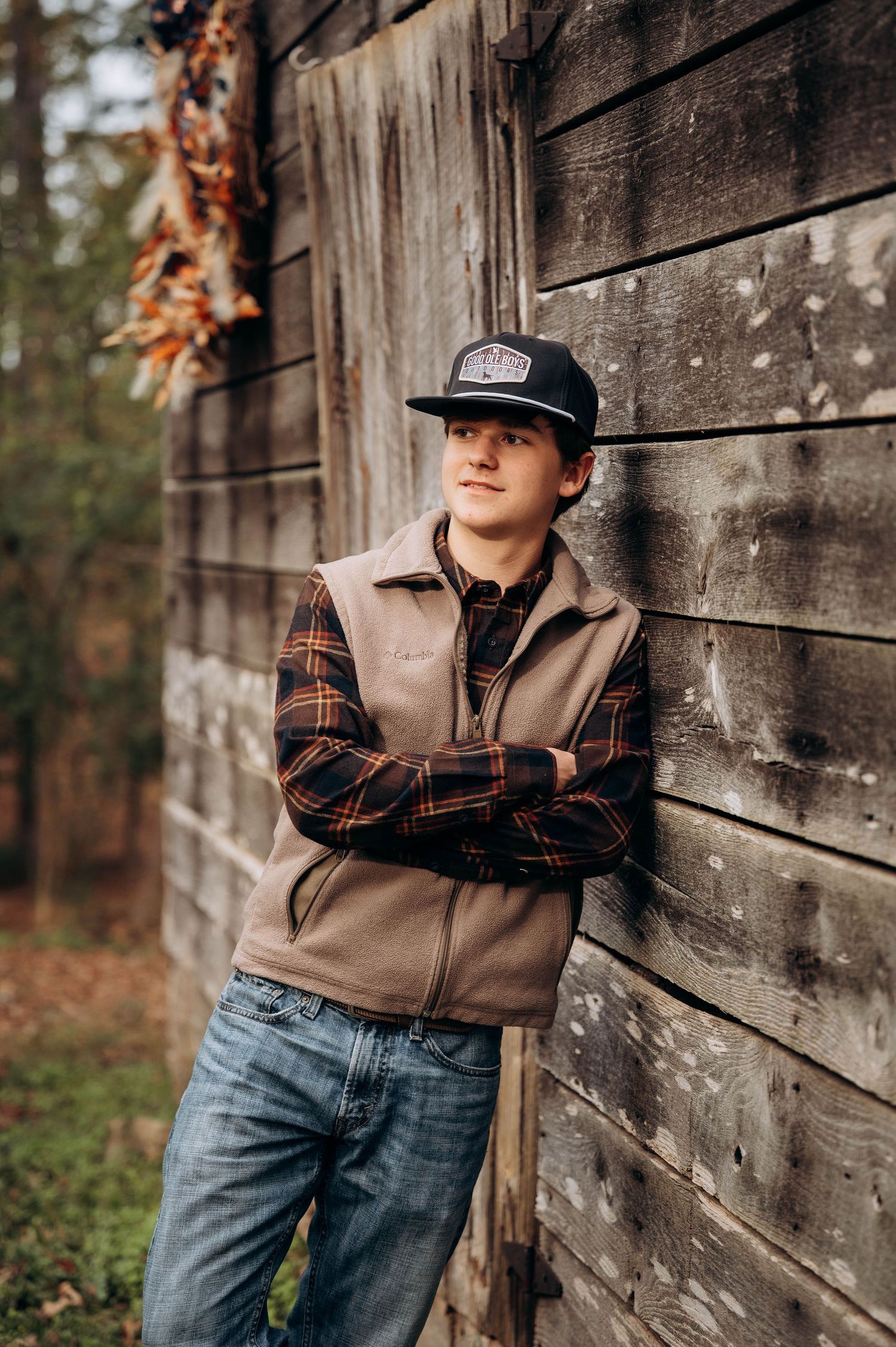 Person in casual workwear leans against rustic wooden barn wall in autumn setting.