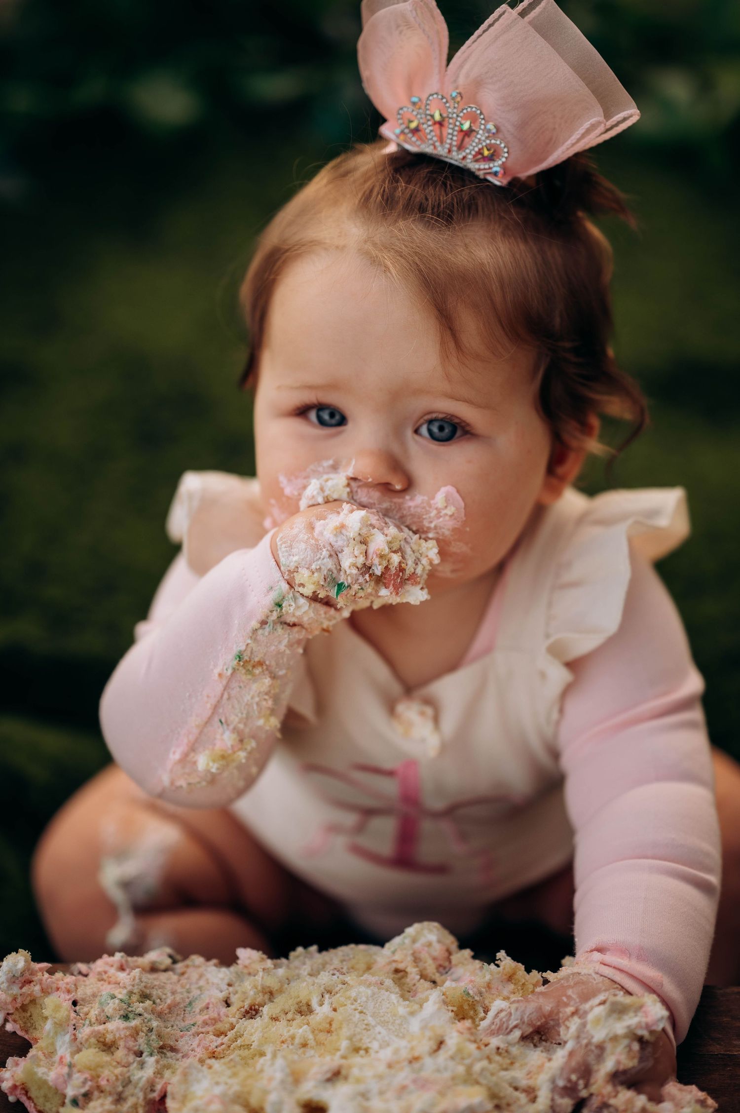 Baby wearing pink crown smashes into birthday cake during first birthday cake smash photoshoot.
