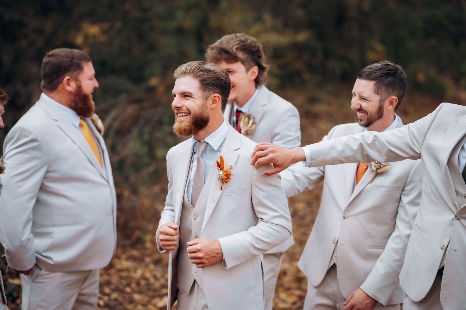 Groomsmen in matching light gray suits share candid moments at fall wedding.