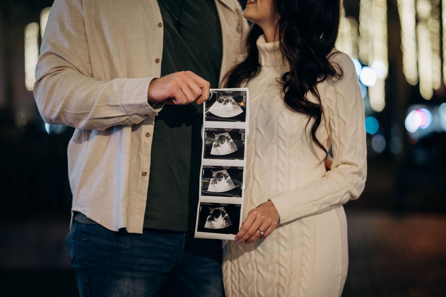 Couple holding ultrasound photos during pregnancy announcement outdoors at night.