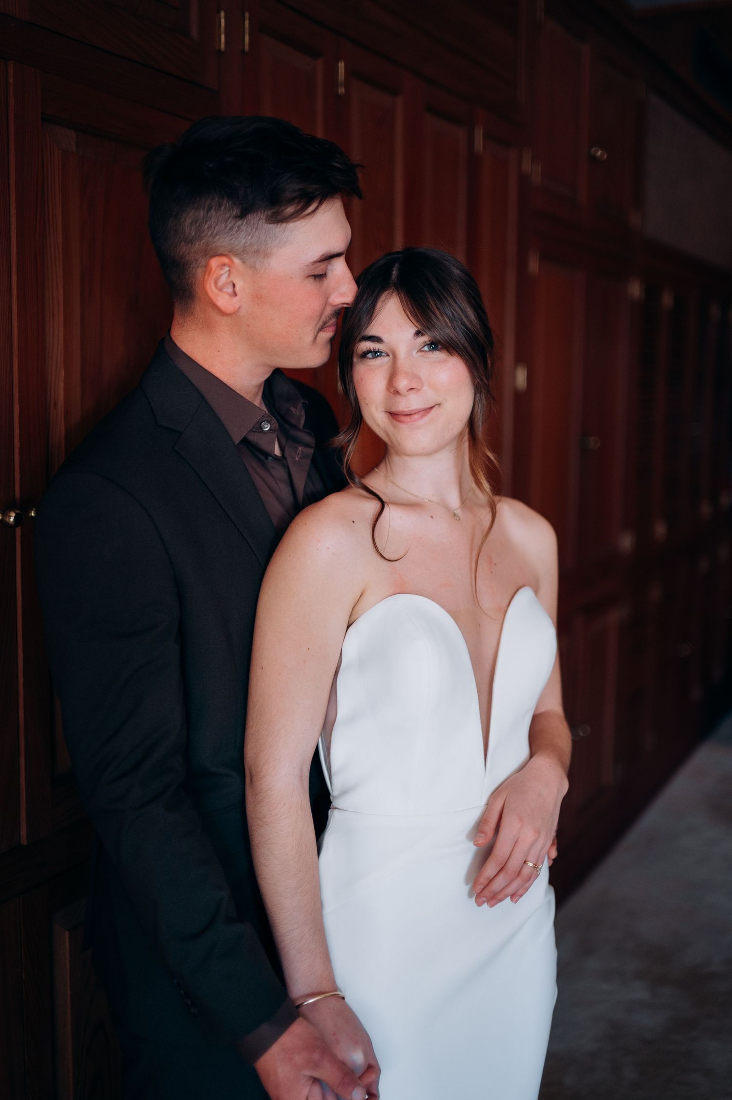 Couple shares intimate first look moment, groom in dark suit embracing bride in white strapless gown.