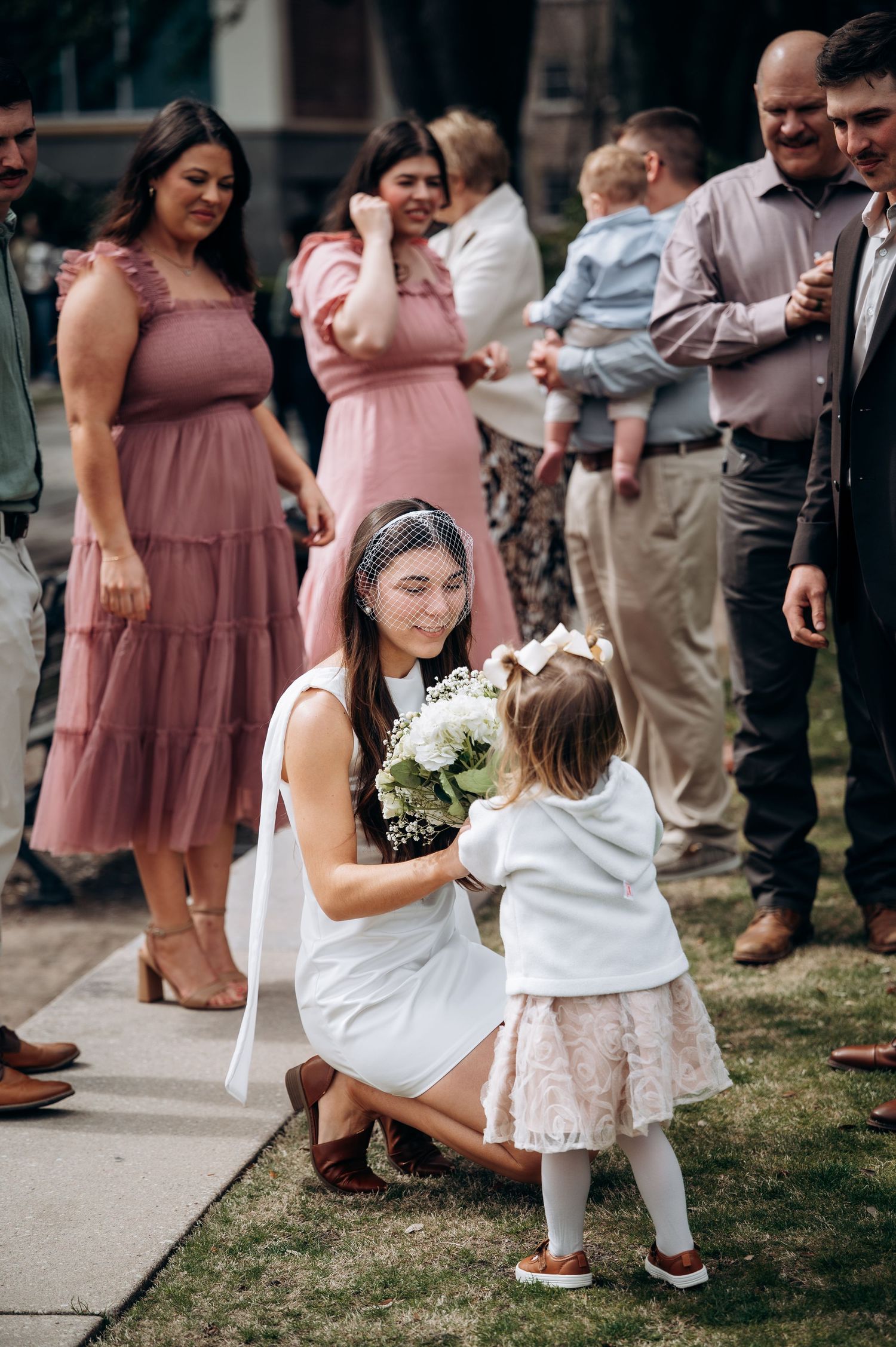 Wedding guests in pink dresses mingle during outdoor reception.