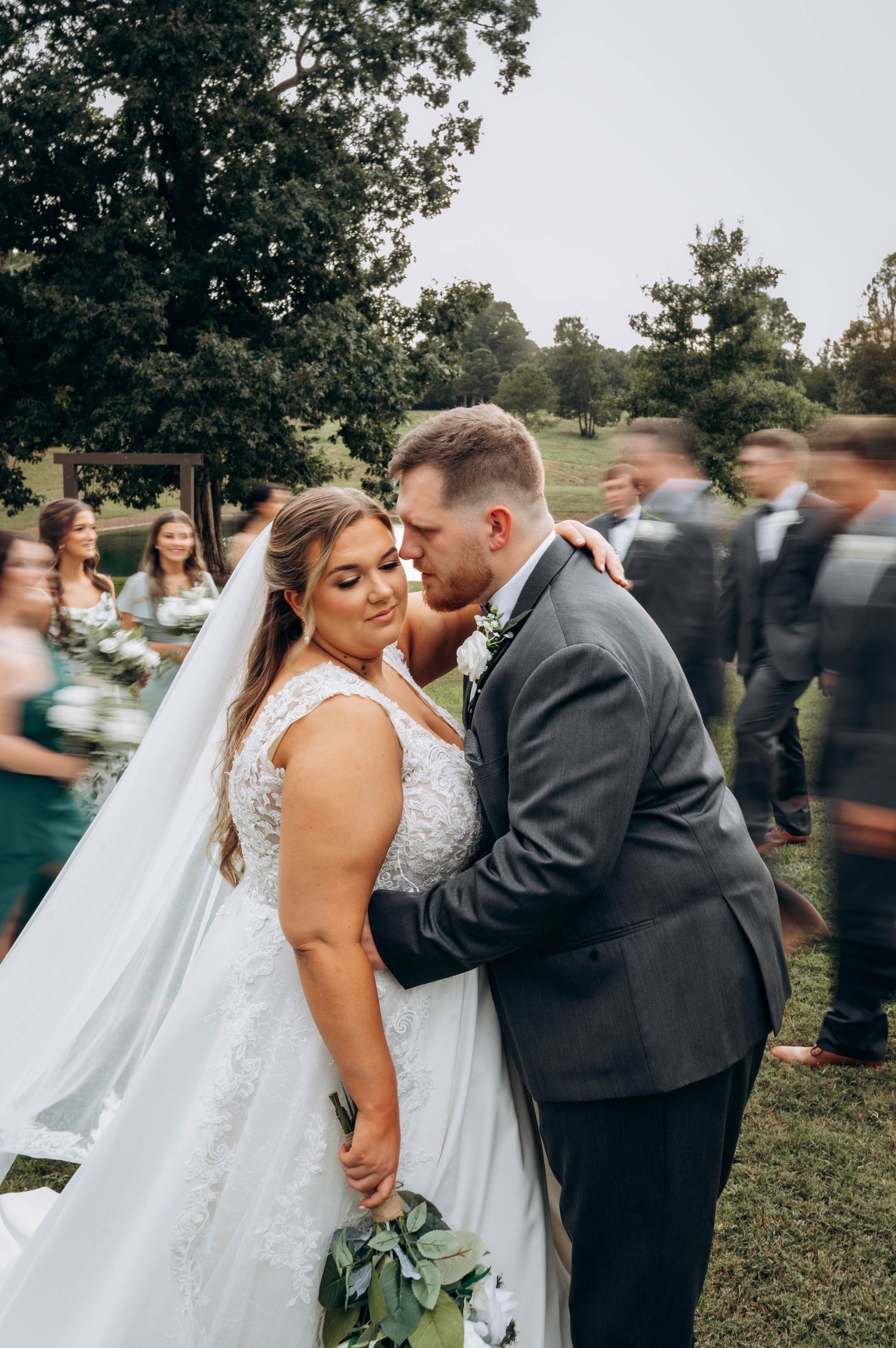 Wedding couple shares intimate moment while guests mingle in background.