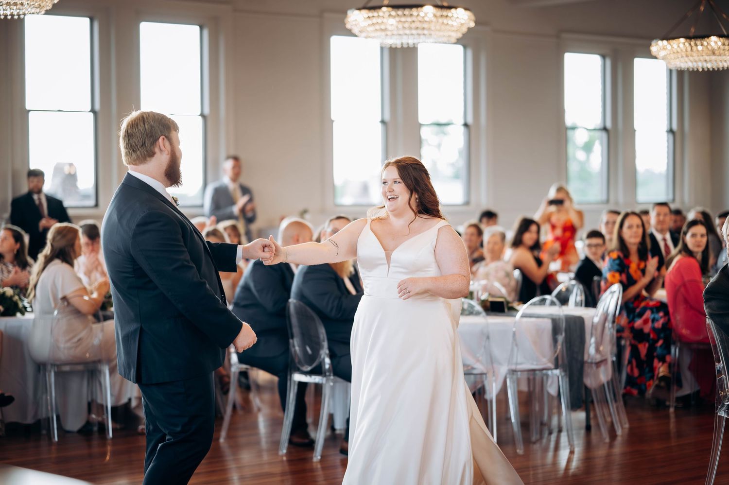 Wedding reception venue with bright windows and guests celebrating on dance floor.