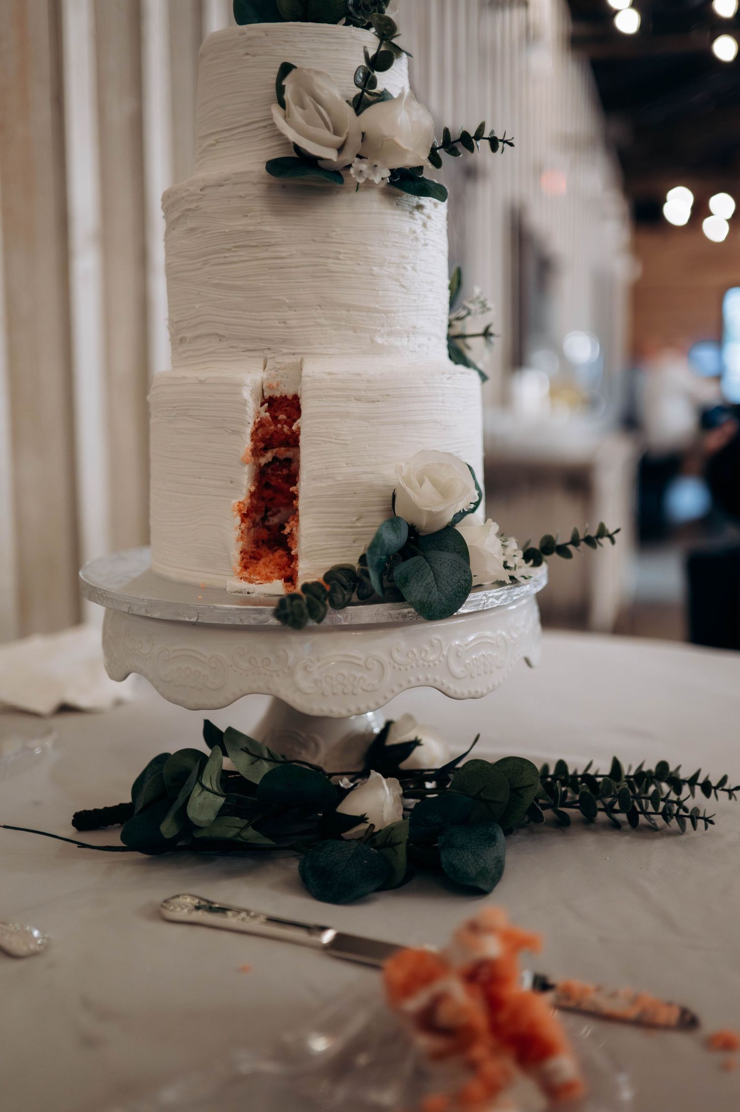 White textured wedding cake decorated with dark green foliage and orange floral accents.