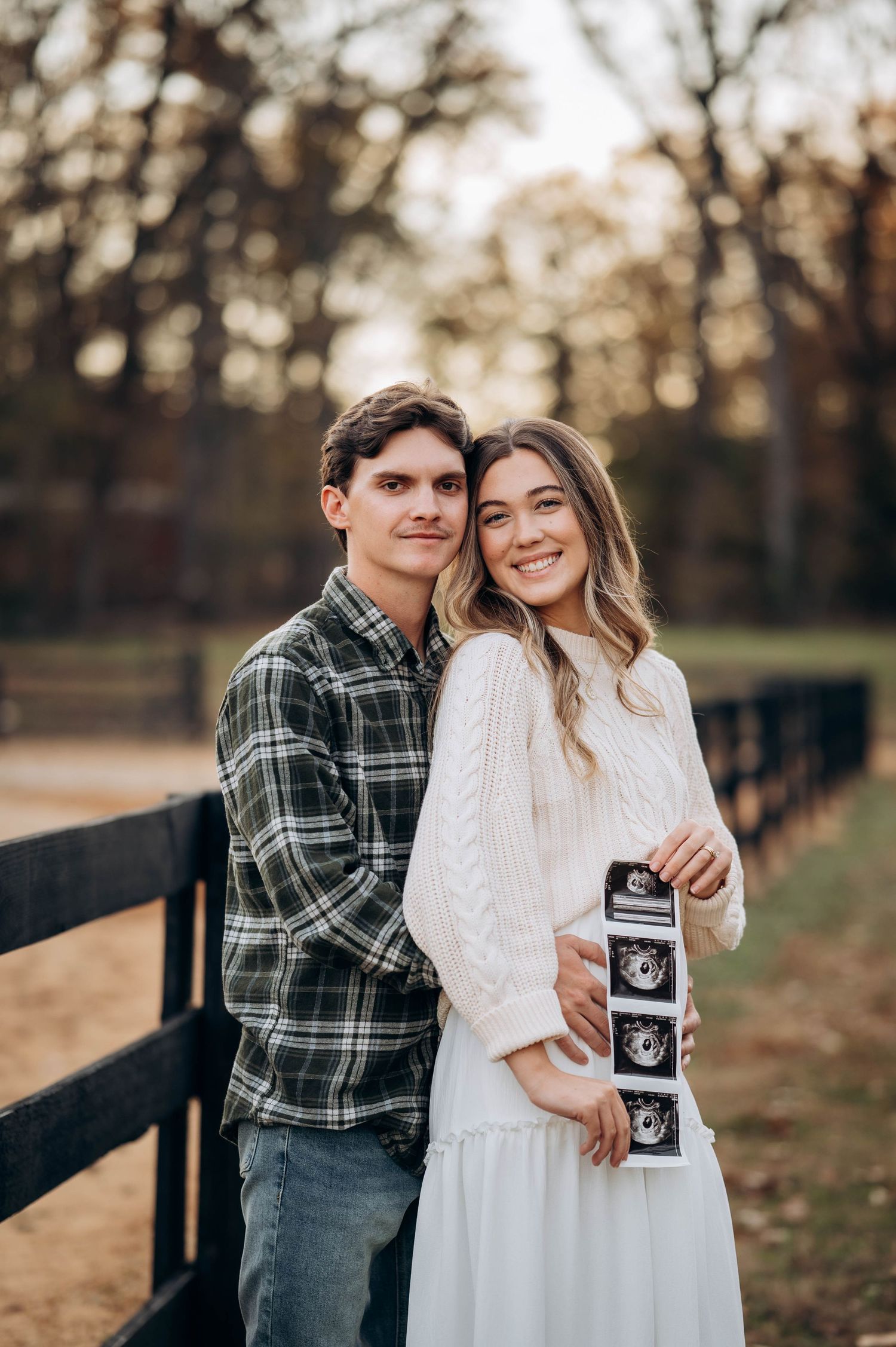 A couple shares a tender moment while holding ultrasound photos during their pregnancy announcement shoot.