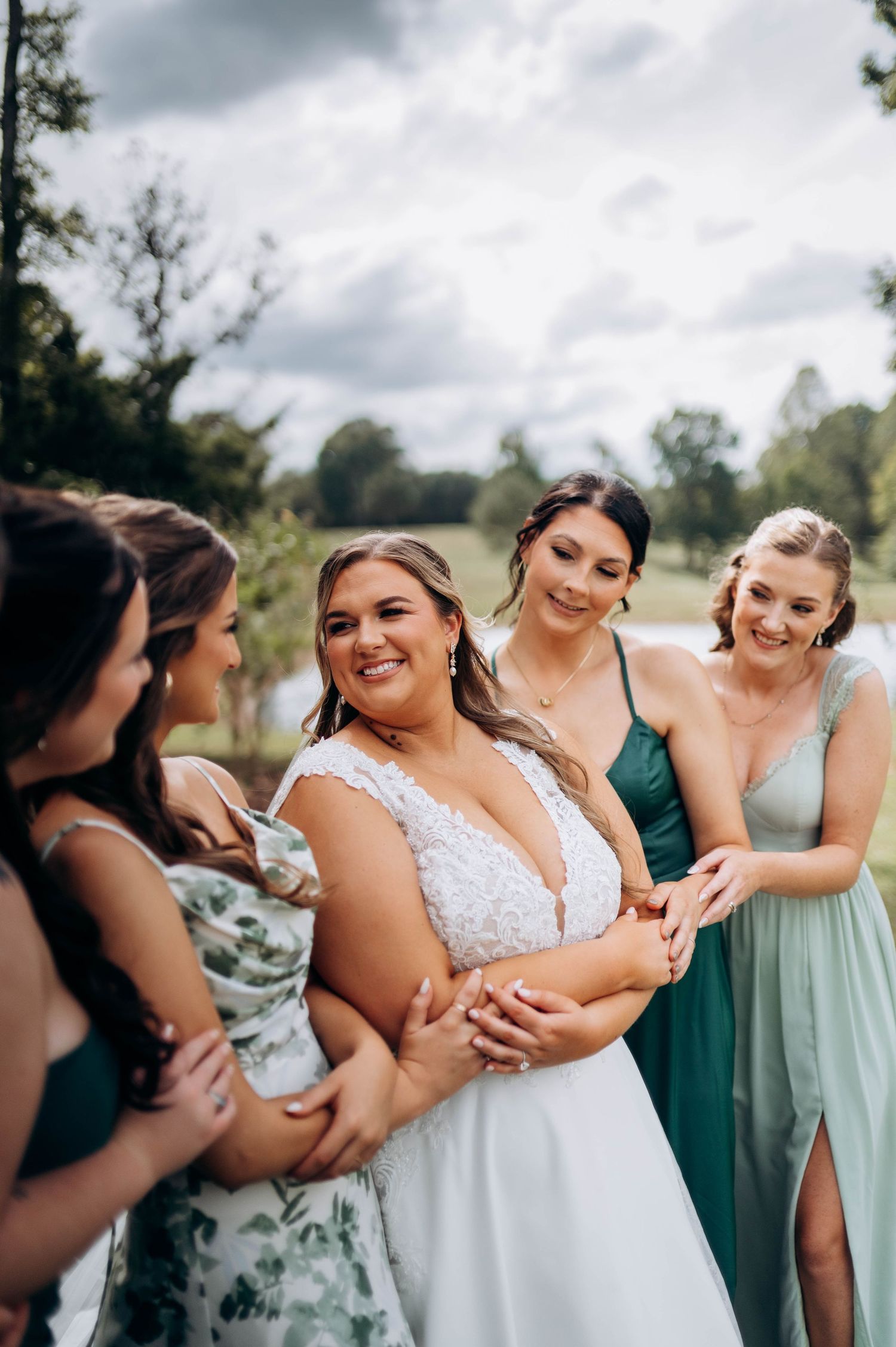 Candid moment of bridesmaids in mixed green dresses laughing with the bride.