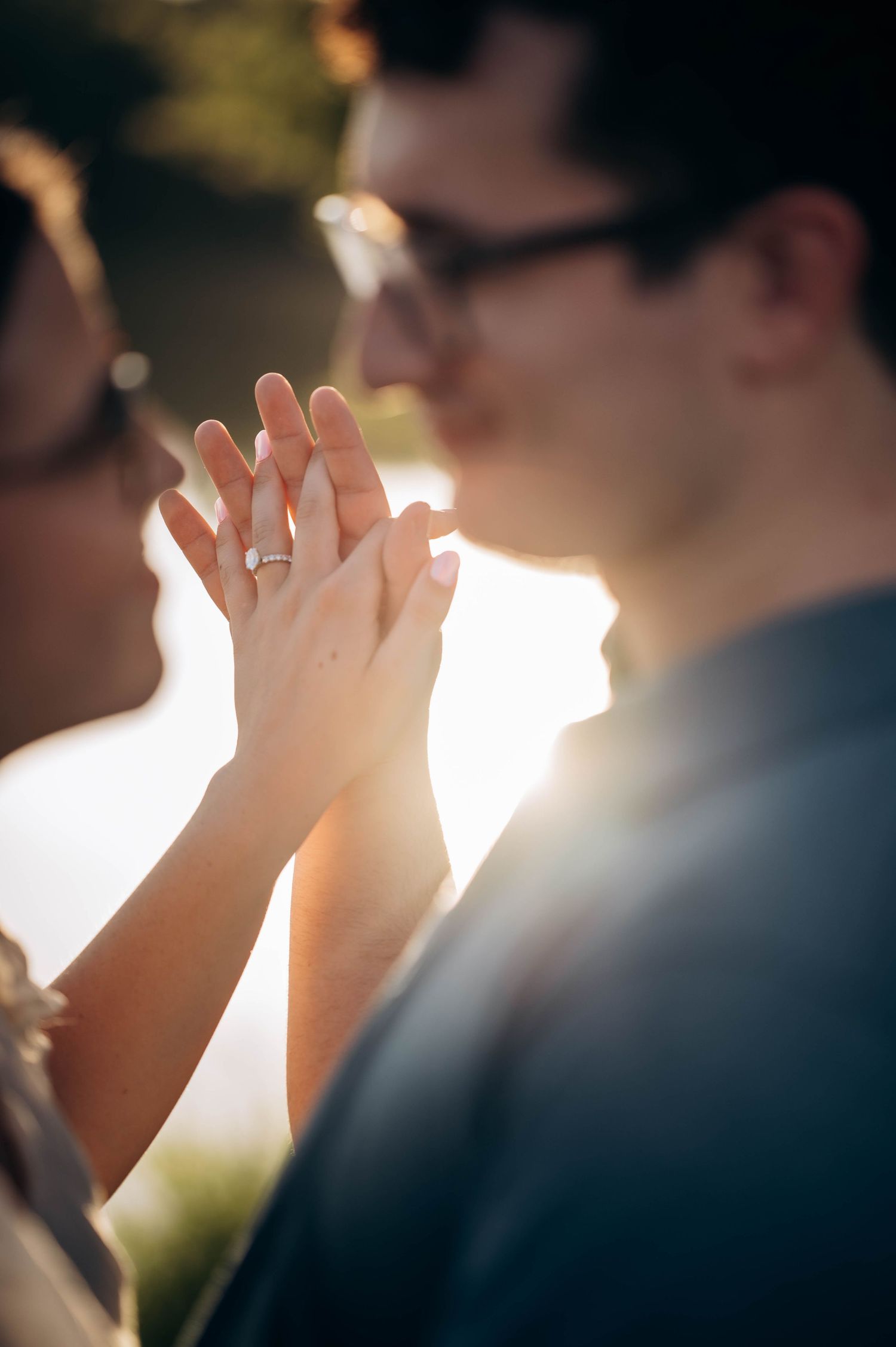 Close-up shot of hands displaying an engagement ring in warm sunset lighting.