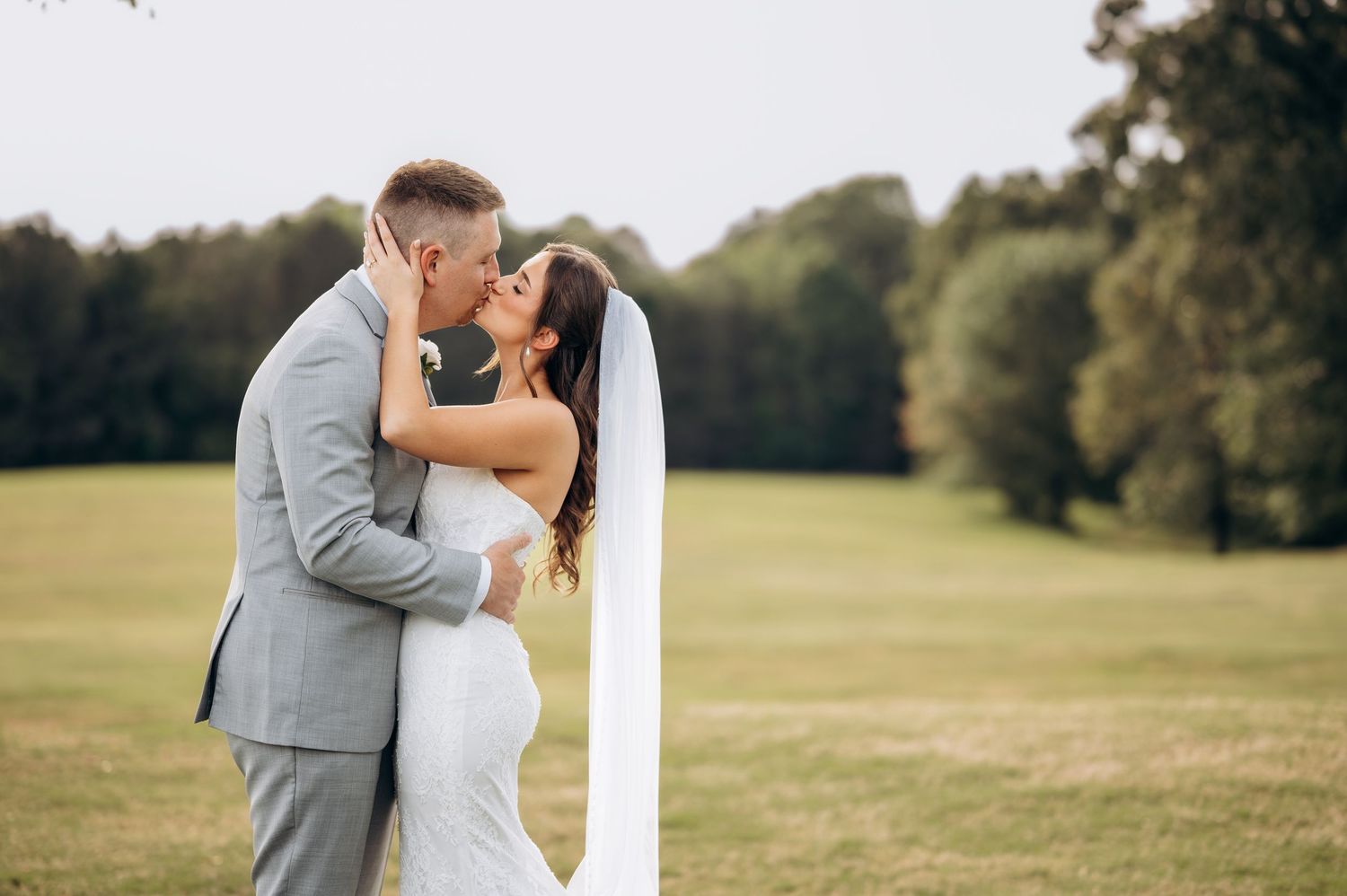 A bride and groom share a romantic kiss on a lush green lawn on their wedding day.